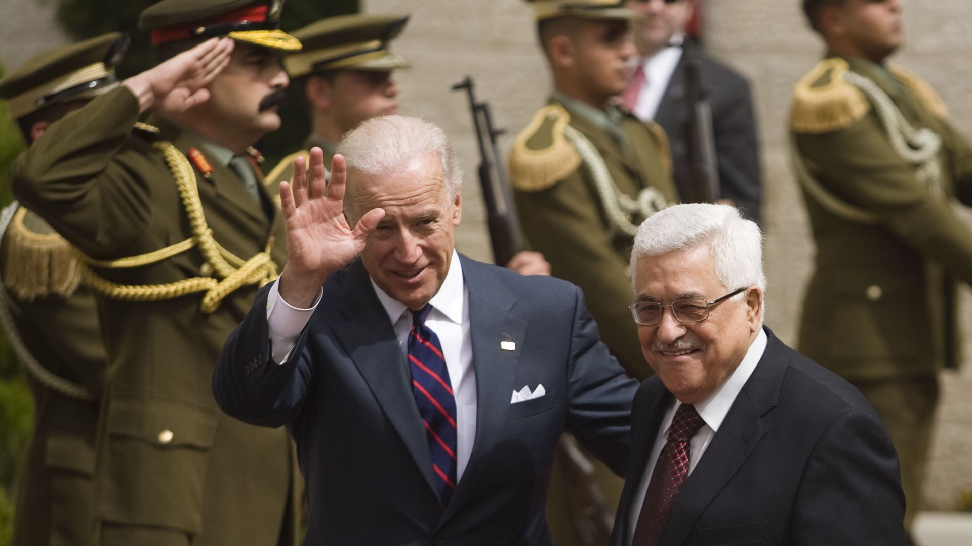 Biden stands with Abbas, both wearing suits and ties, in front of saluting military figures 