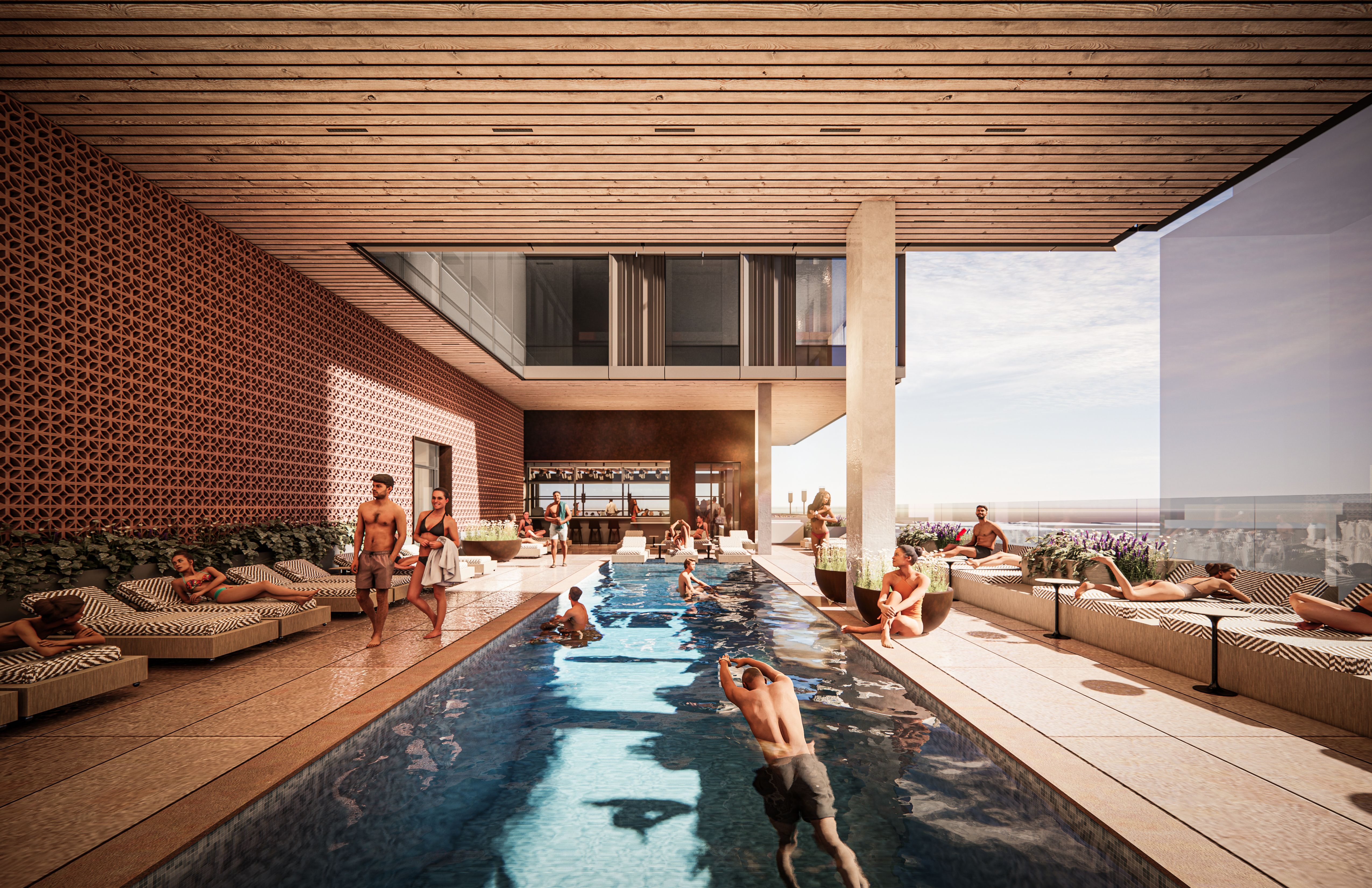 Outdoor pool area beneath a wooden slatted ceiling; left wall features a lattice pattern, with sun loungers and people in swimsuits around a long rectangular pool, glass railing and modern building in background.