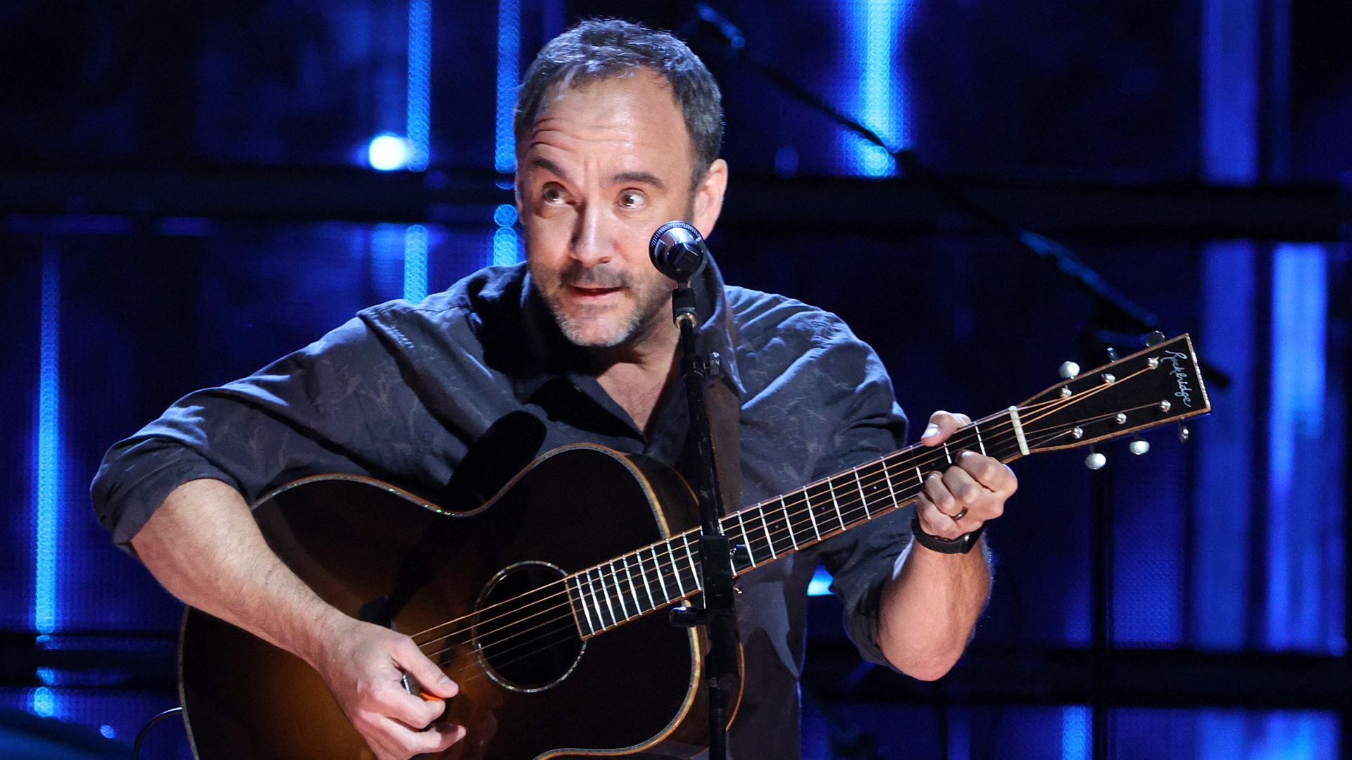 Dave Matthews performs on stage with an acoustic guitar. 
