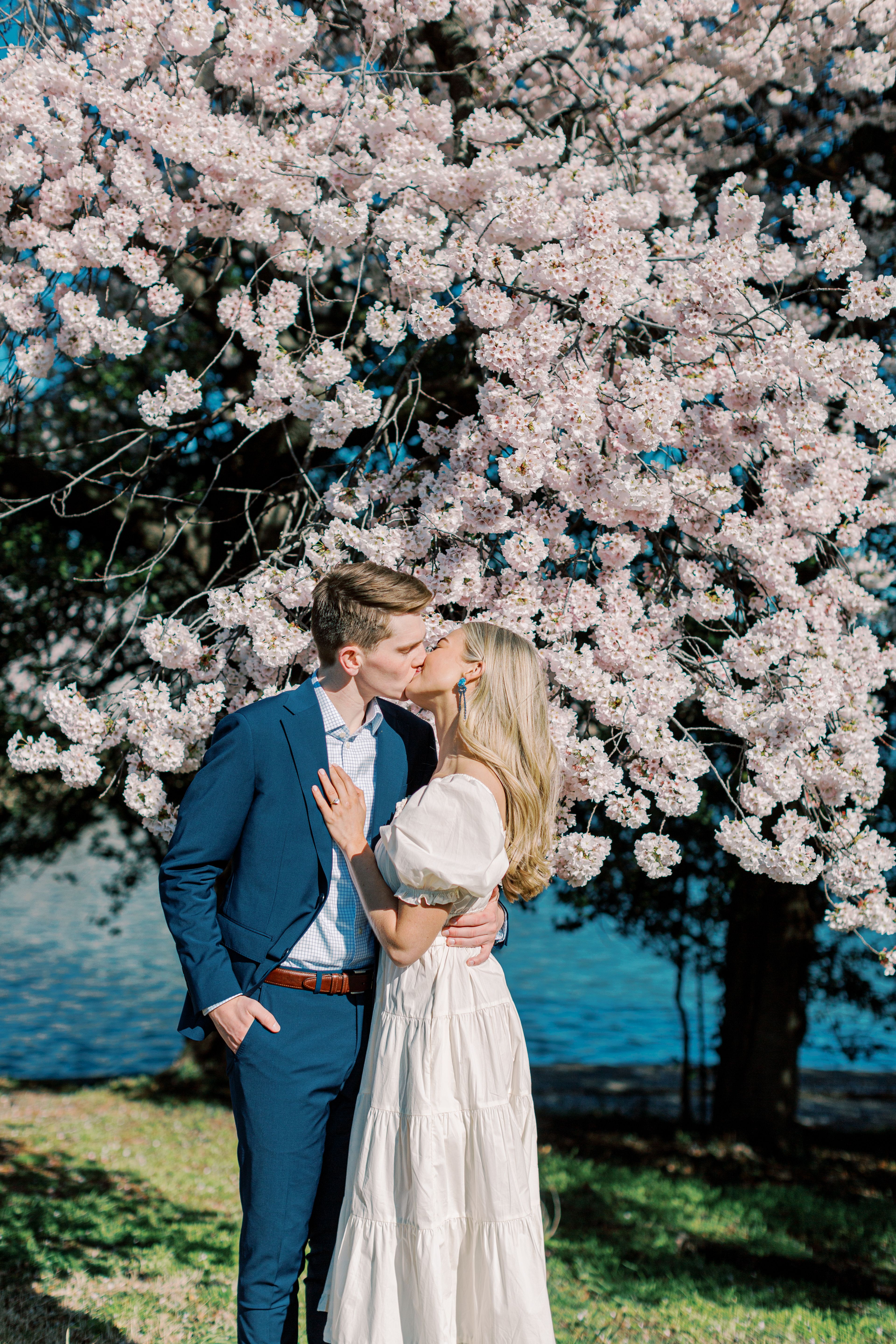 A couple kisses in front of cherry blossoms.