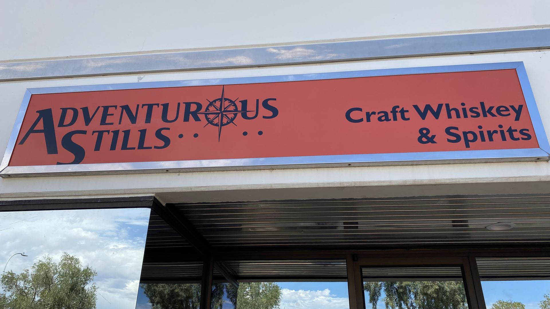 A rectangular orange sign for Adventurous Stills craft whiskey and spirits.
