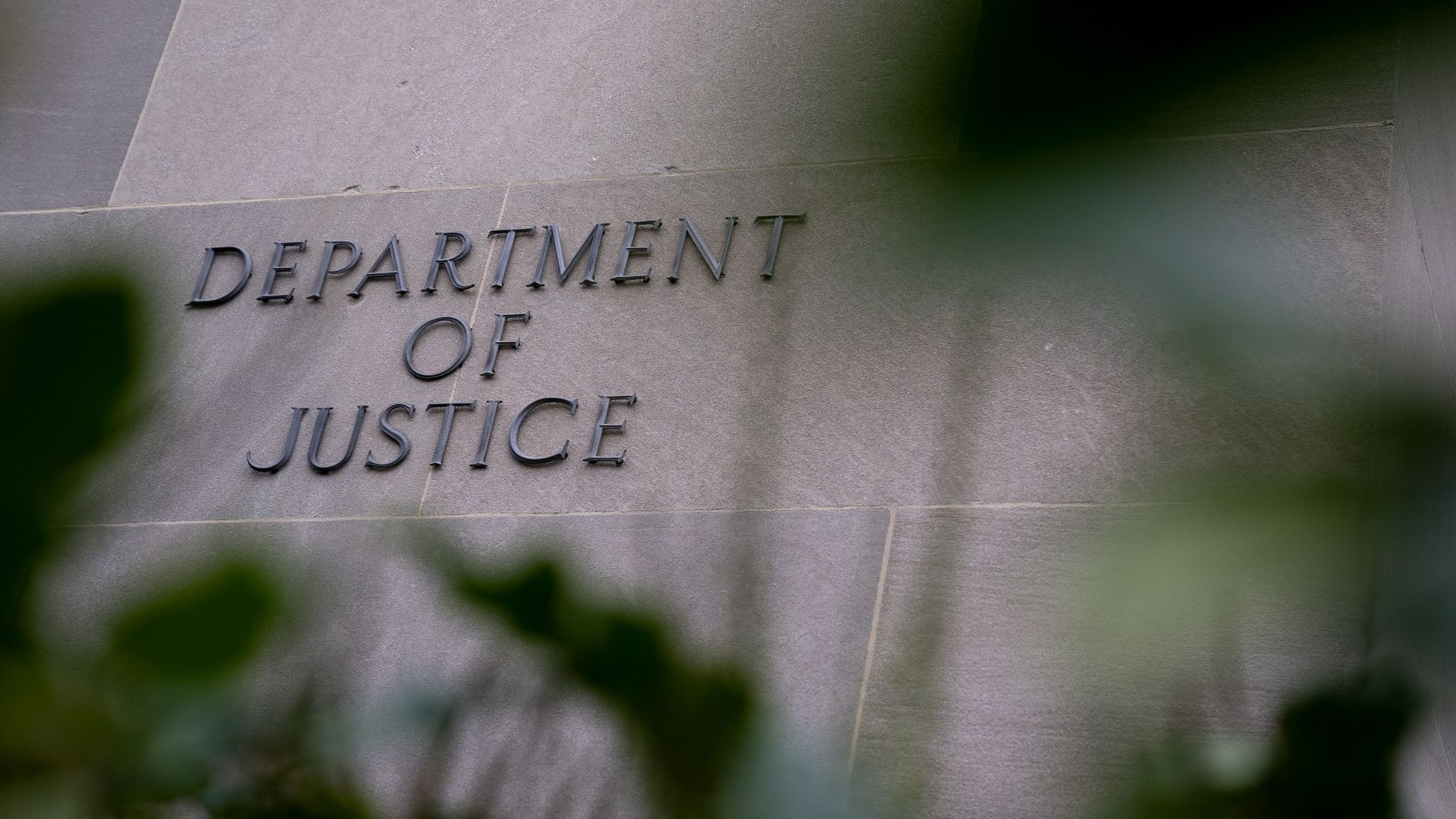Photo of the Department of Justice building with green leaves in the foreground