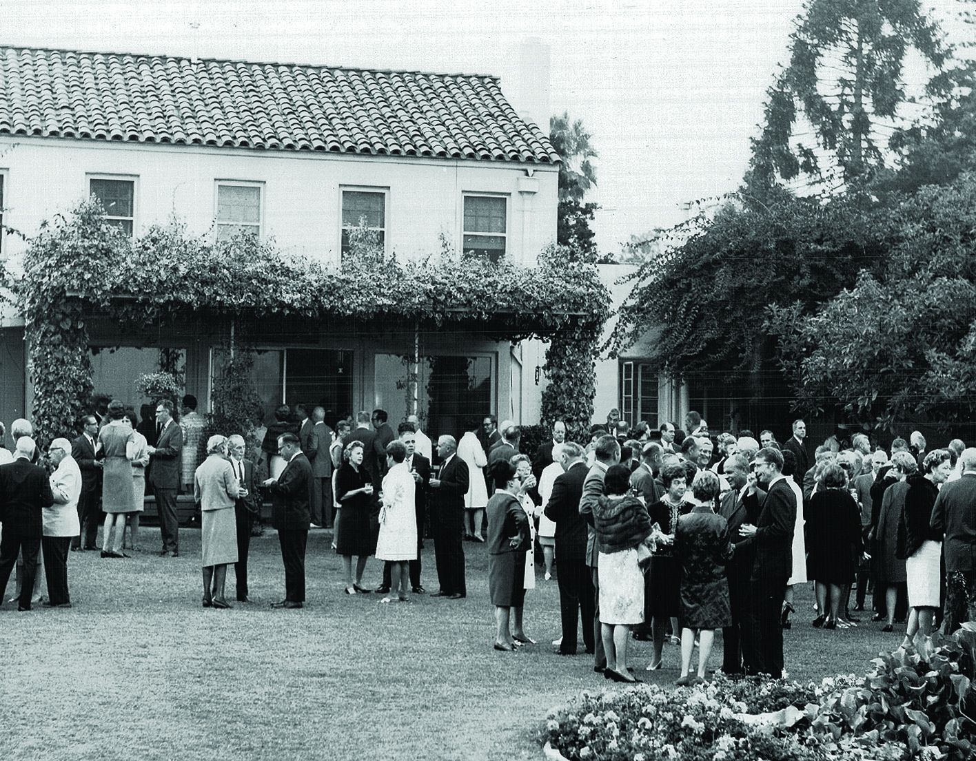A black and white photo of people gathered outside for a fancy garden party. 