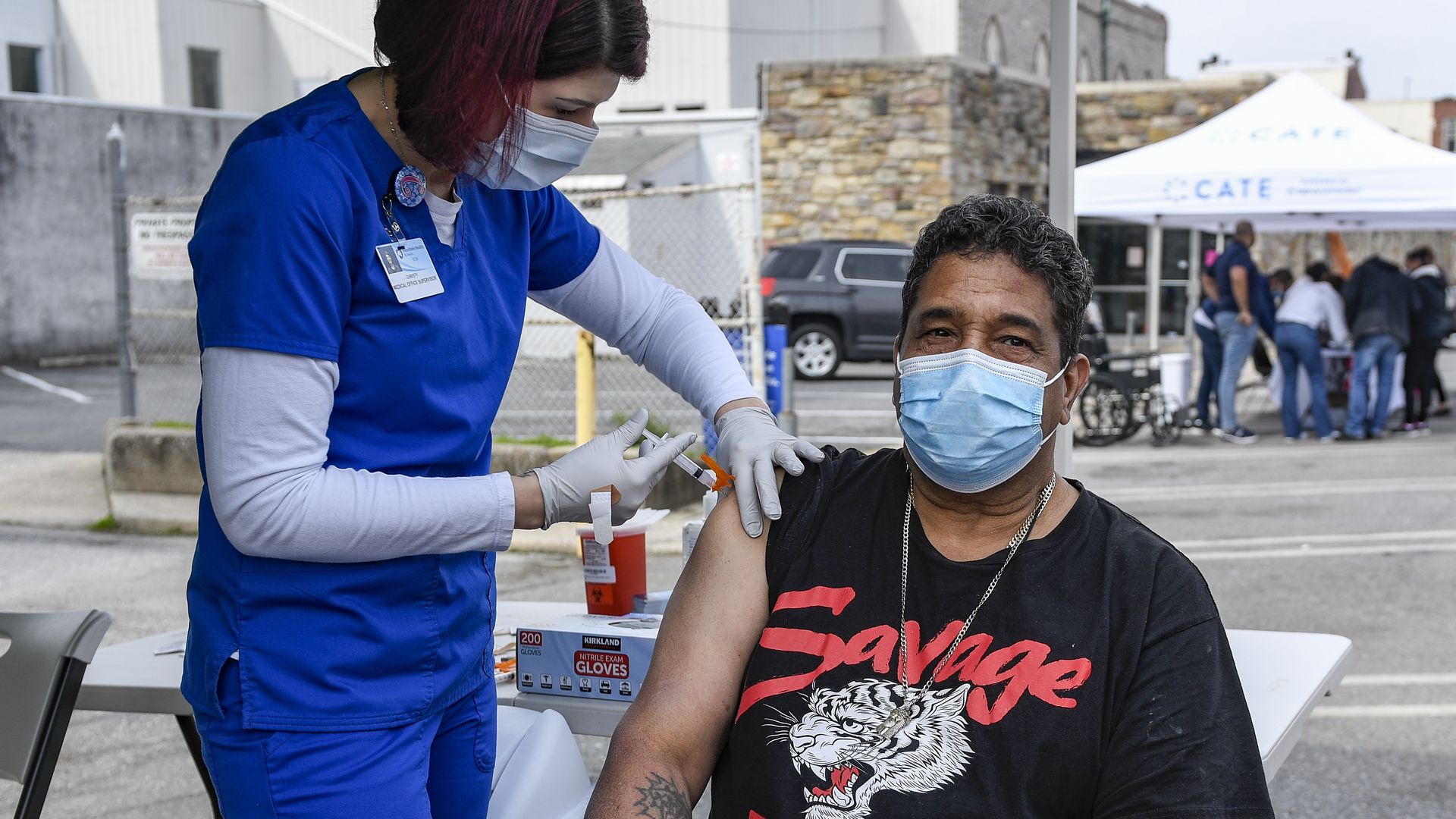Photo of a masked person getting their vaccine shot in their right arm outside in an open area