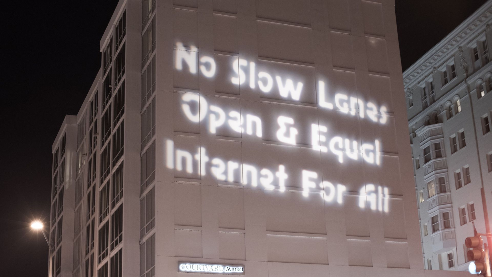 The words "No Slow Lanes Open & Equal Internet For All" projected in white on the side of a building at night