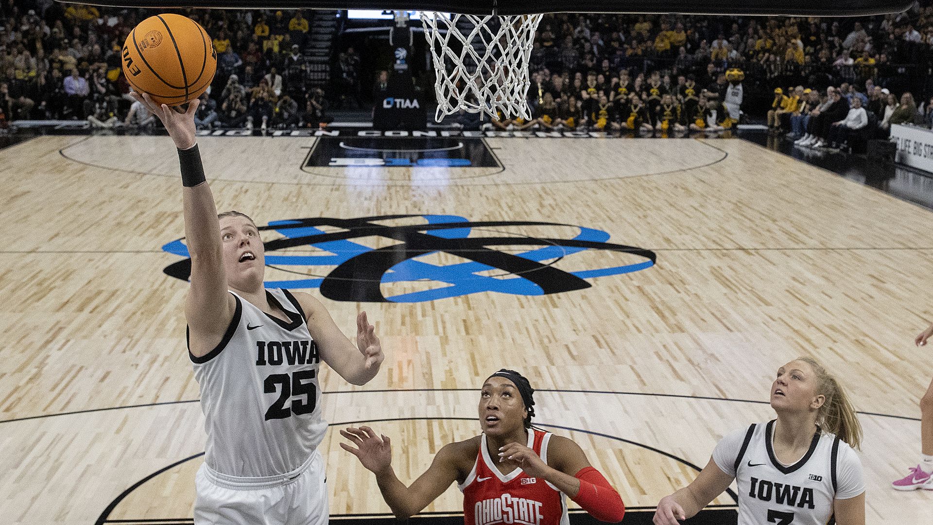 A woman throws a basketball into a hoop as two other women attempt to block her.