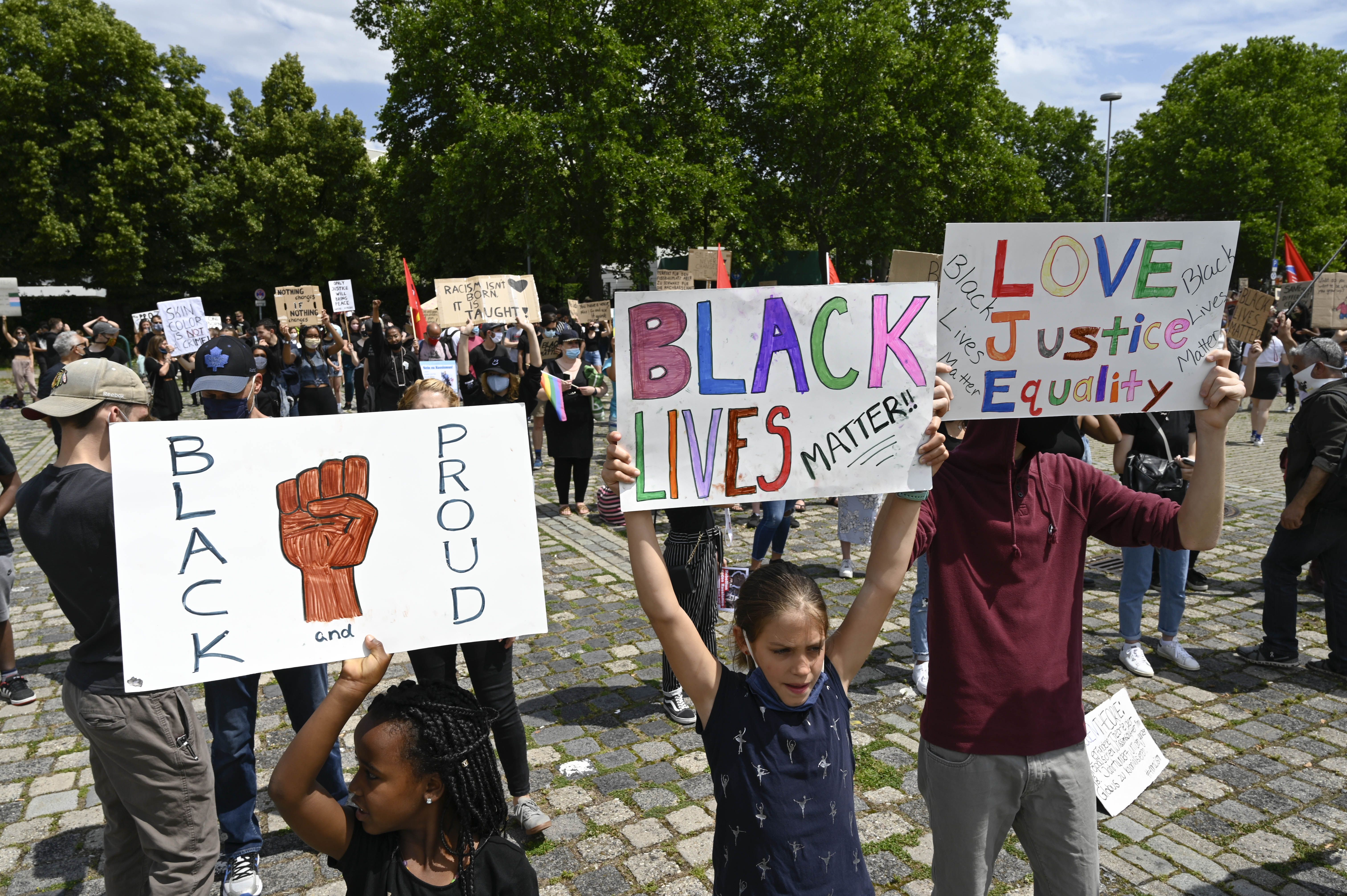 Children hold three signs that read "Black and Proud," "Black Lives Matters" and "Love Justice Equality"