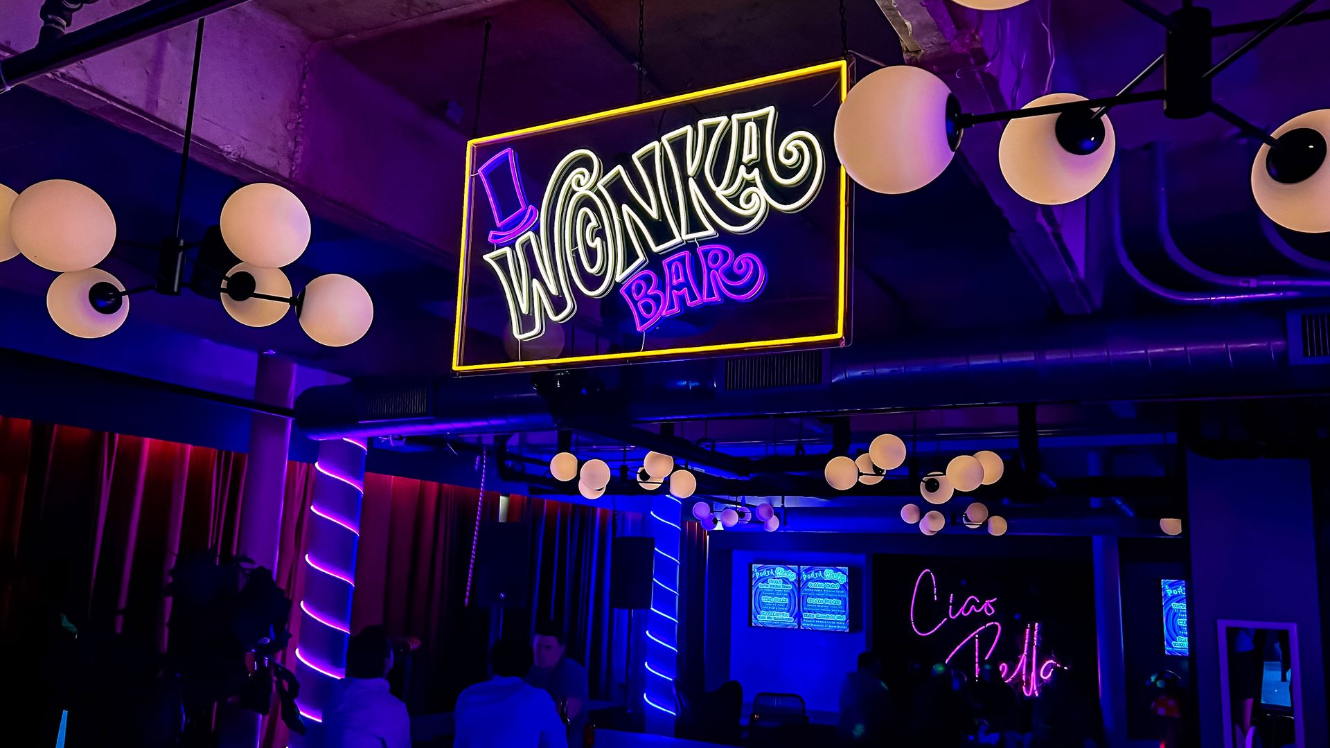 A dim room with illuminated by bulbous pendant lighting and a neon sign that says "Wonka Bar."