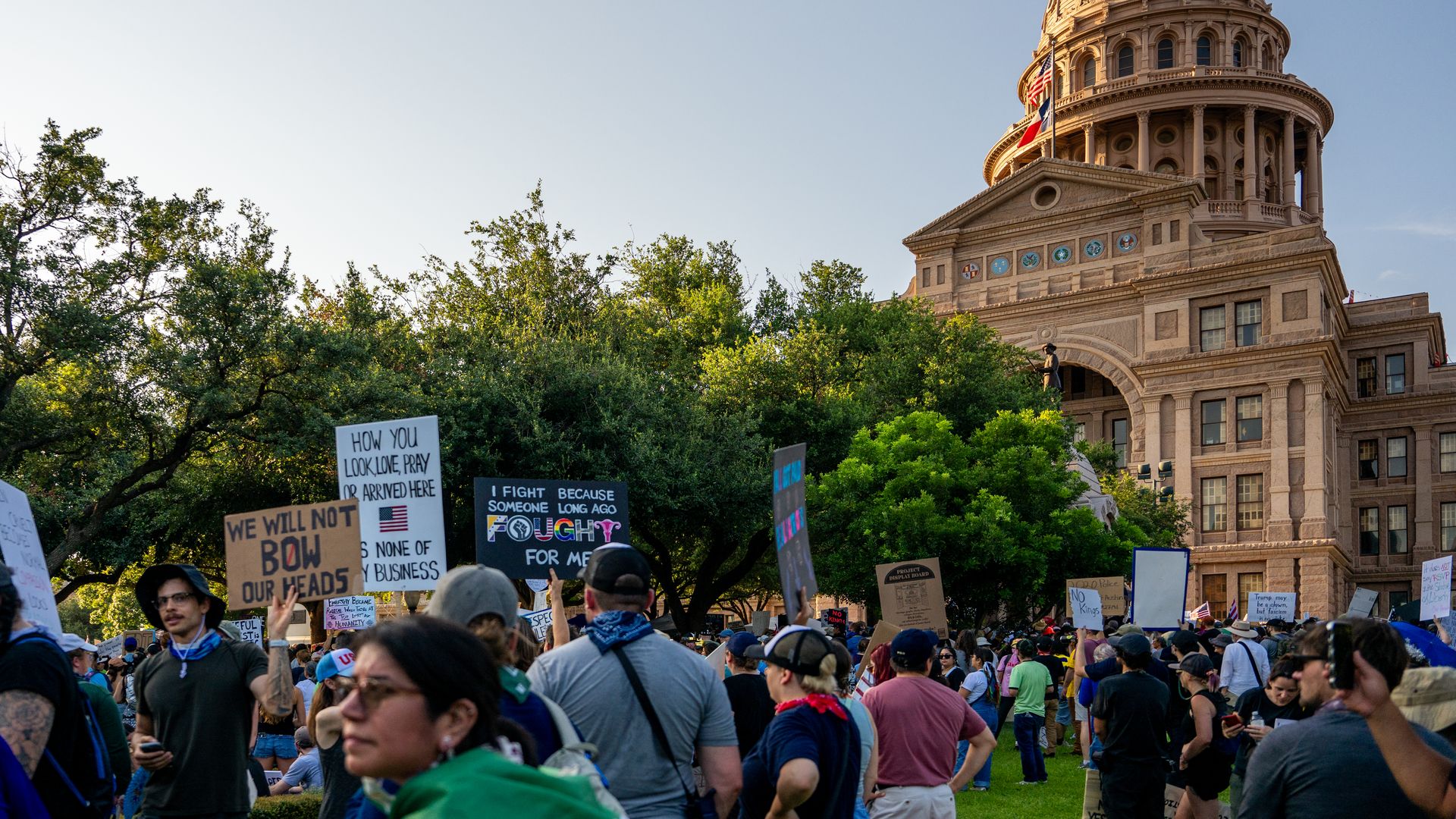Dozens of people, many holding signs, stand in front of a government building