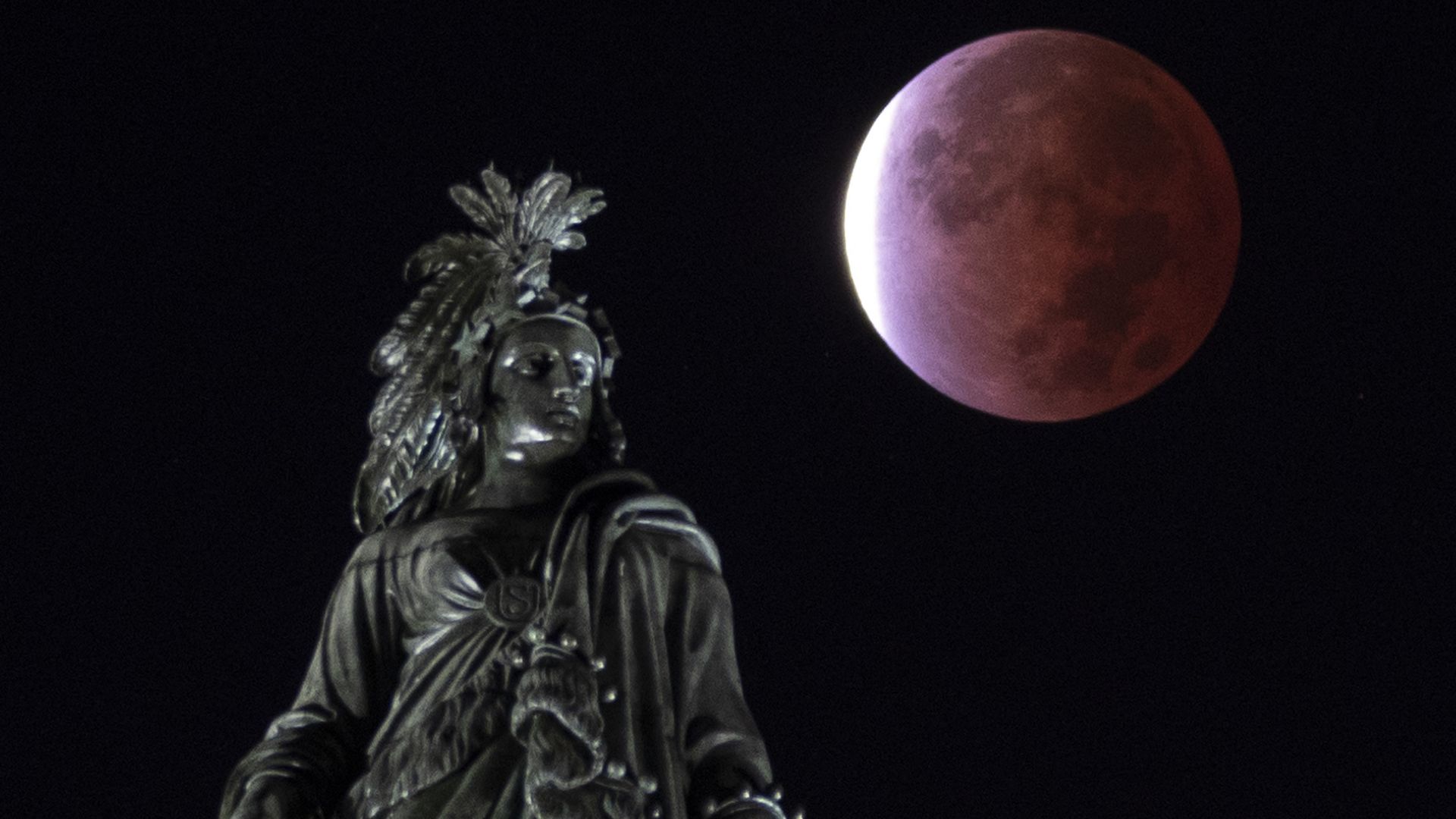 The moon in an eclipsed state is seen rising behind the statue atop the U.S. Capitol.