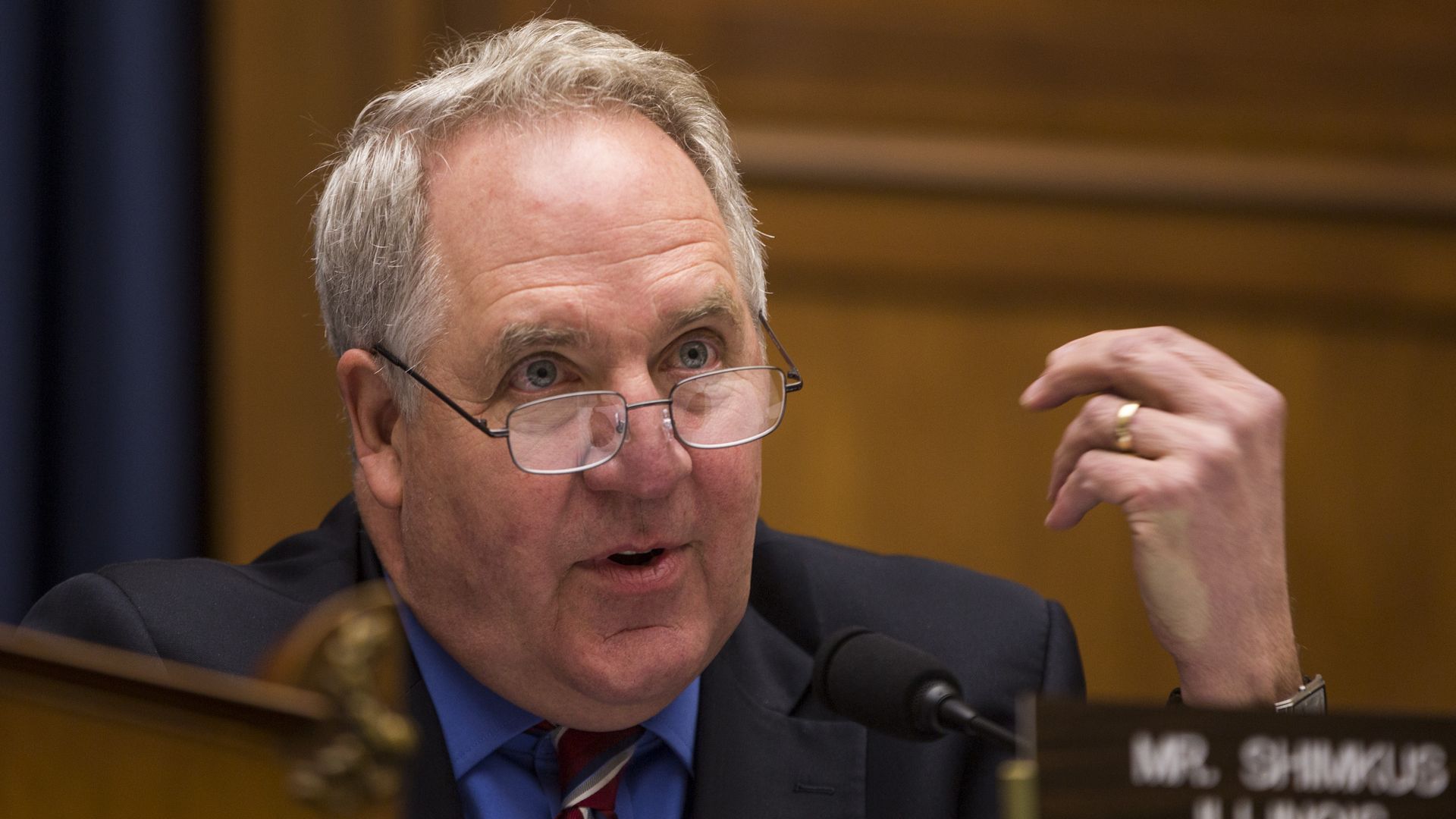 In this image, Rep. Shimkus is sitting and speaking while wearing glasses and gesturing with one hand.