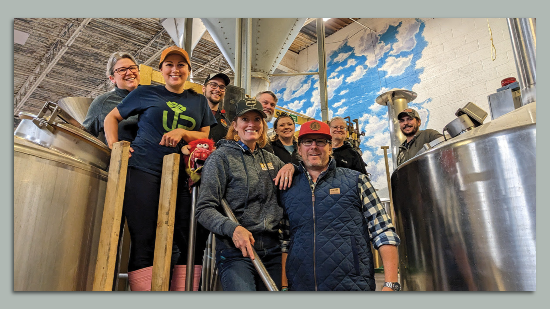 A group of people smile for the camera amidst brewing equipment. 