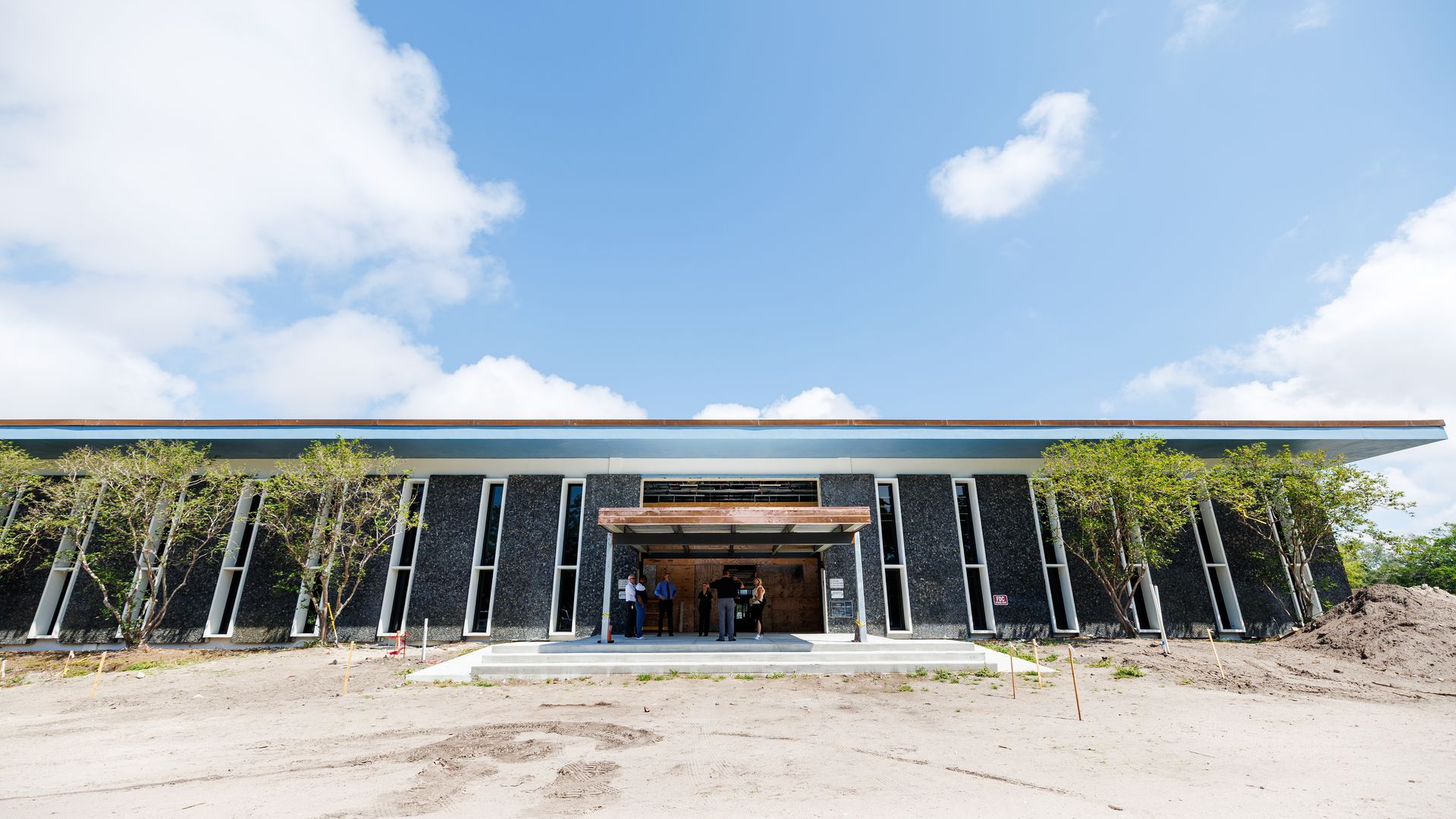 A long, gray building with narrow windows surrounded by dirt. 