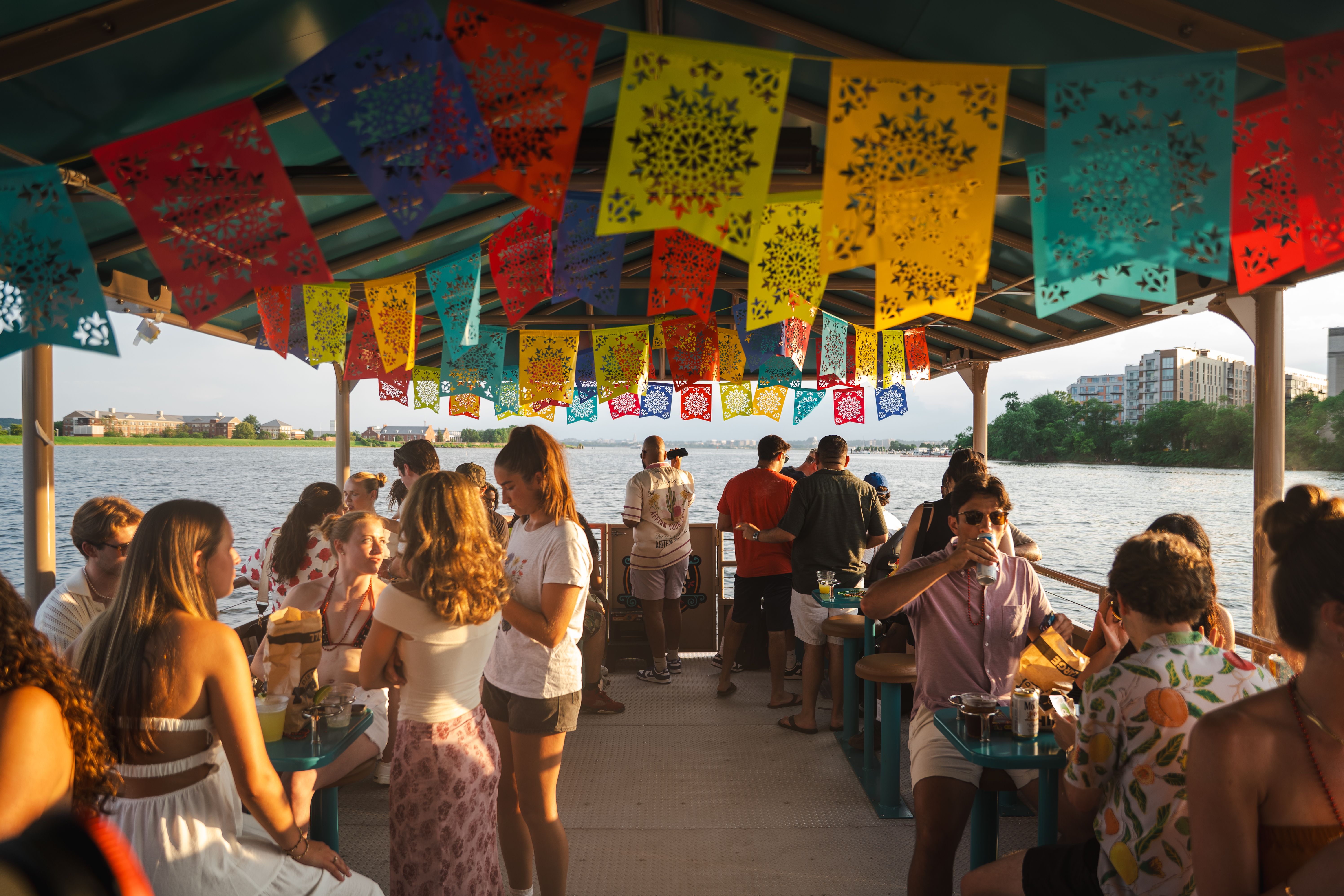 A floating Cantina Cruises boat with colorful flags hanging down and people eating and drinking 