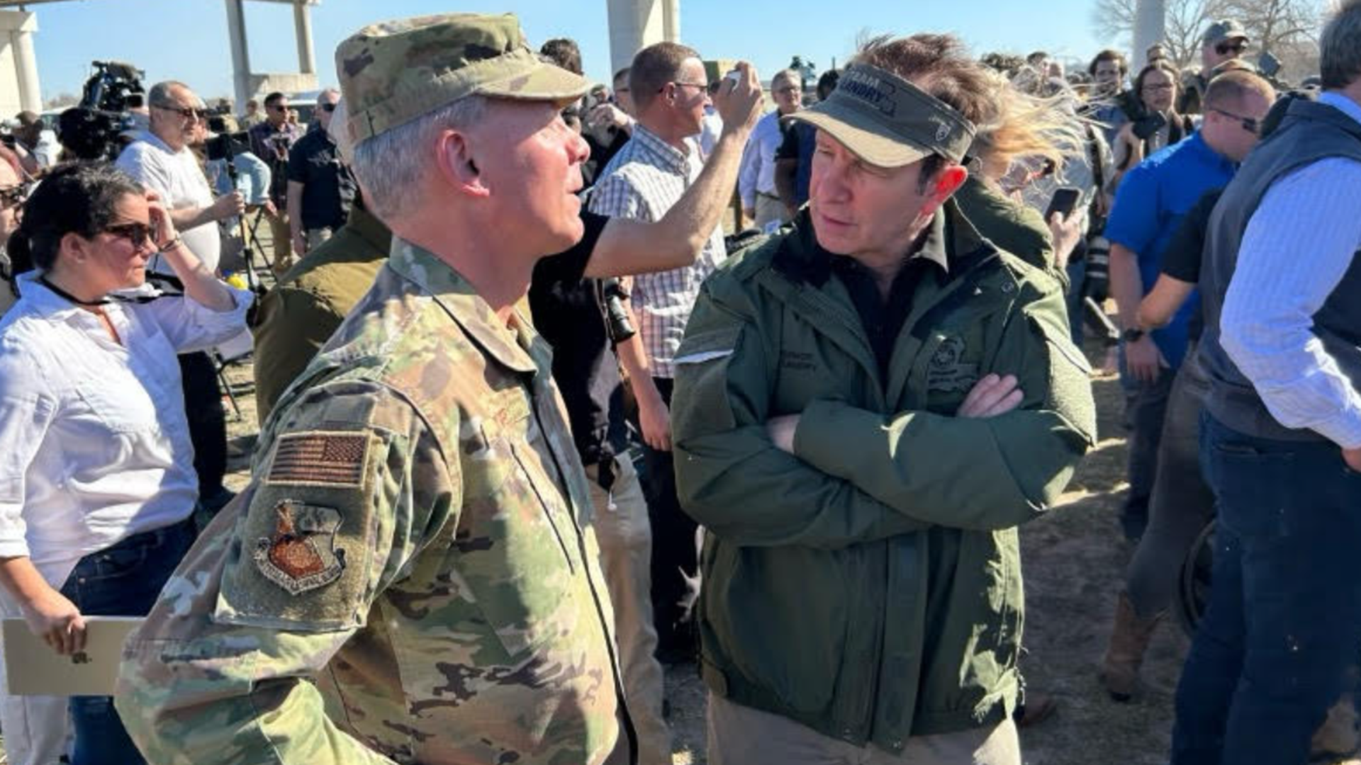 Gov. Jeff Landry, arms crossed, speaks to a man in military fatigues.
