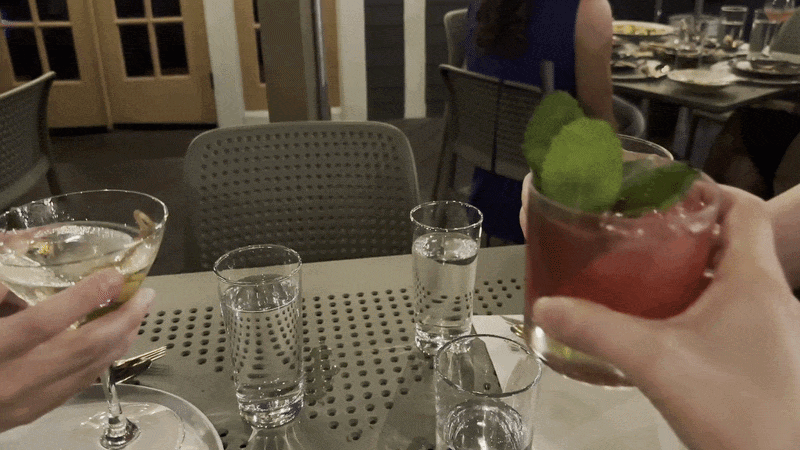 Three hands holding cocktails reach toward each other in a toast.