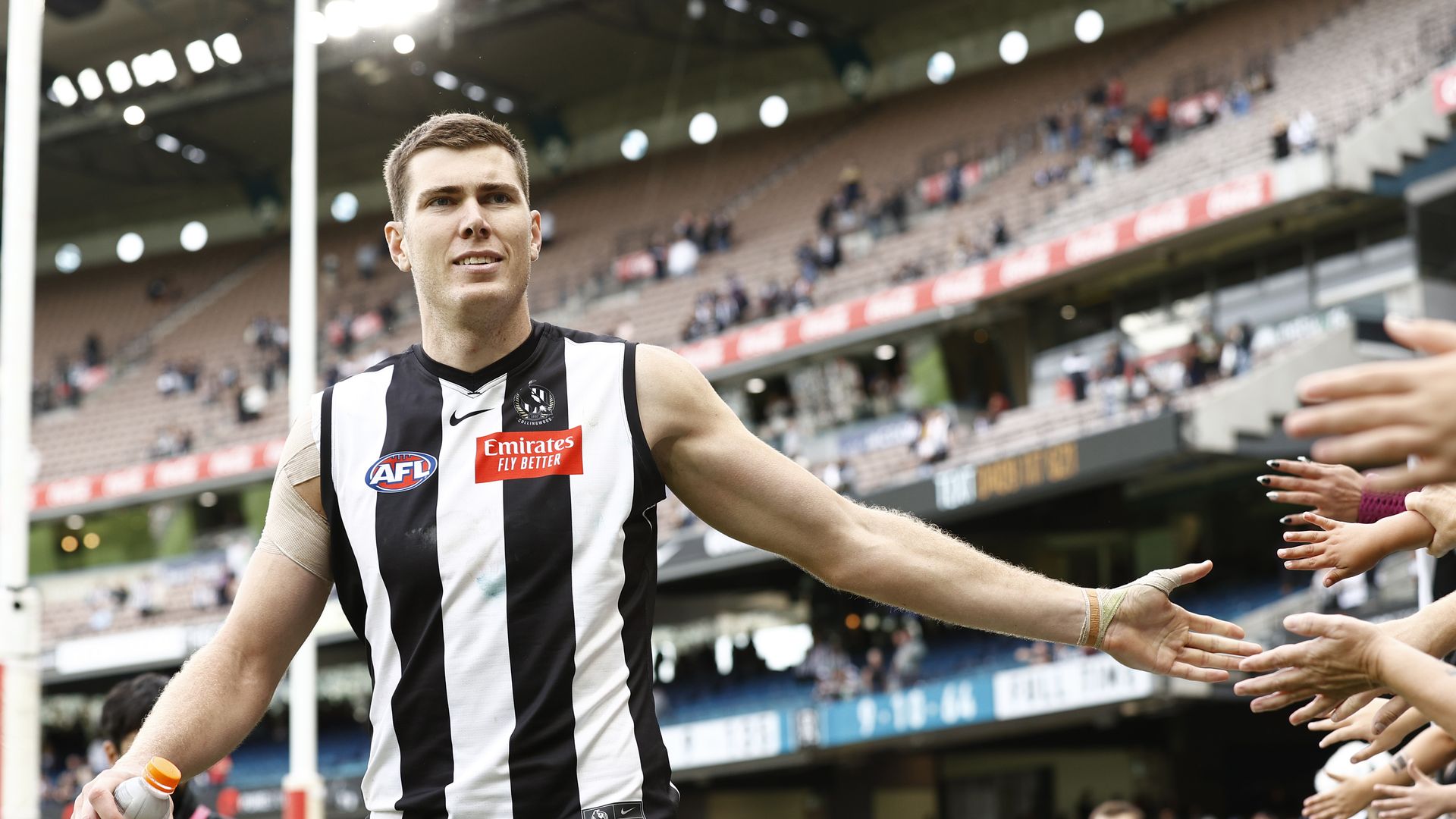 A giant man in an Australian rules football uniform is slapping hands with fans