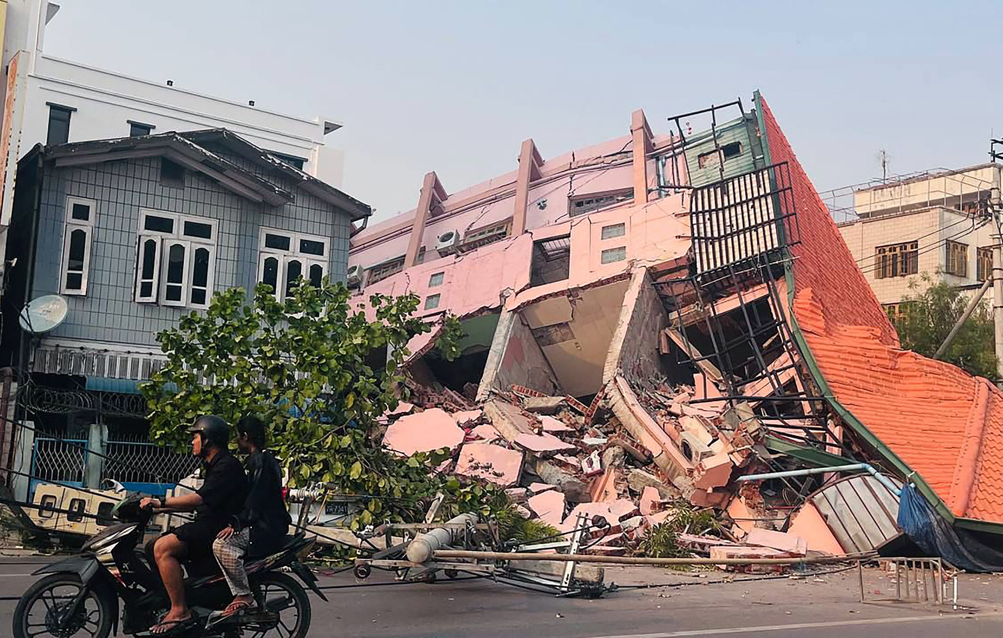 People drive on a motorbike past a collapsed building in Mandalay on March 28, 2025, after an earthquake in central Myanmar. 
