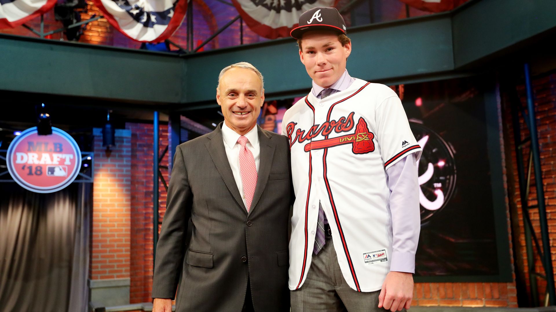 In this image, Carter Stewart and commissioner Rob Manfred stand next to each other on a stage with a brick wall.