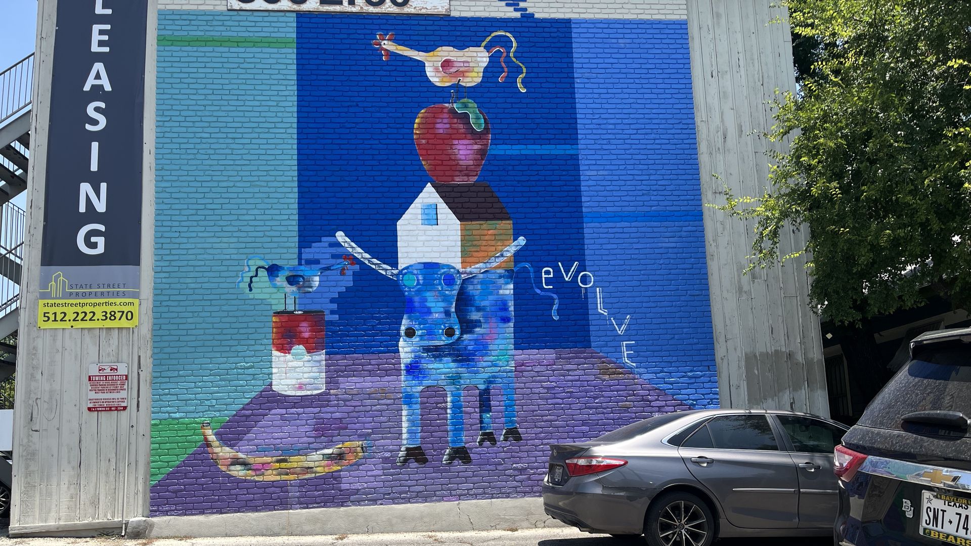 A mural somewhere in Austin with an apple on top of a house on top of a blue longhorn.