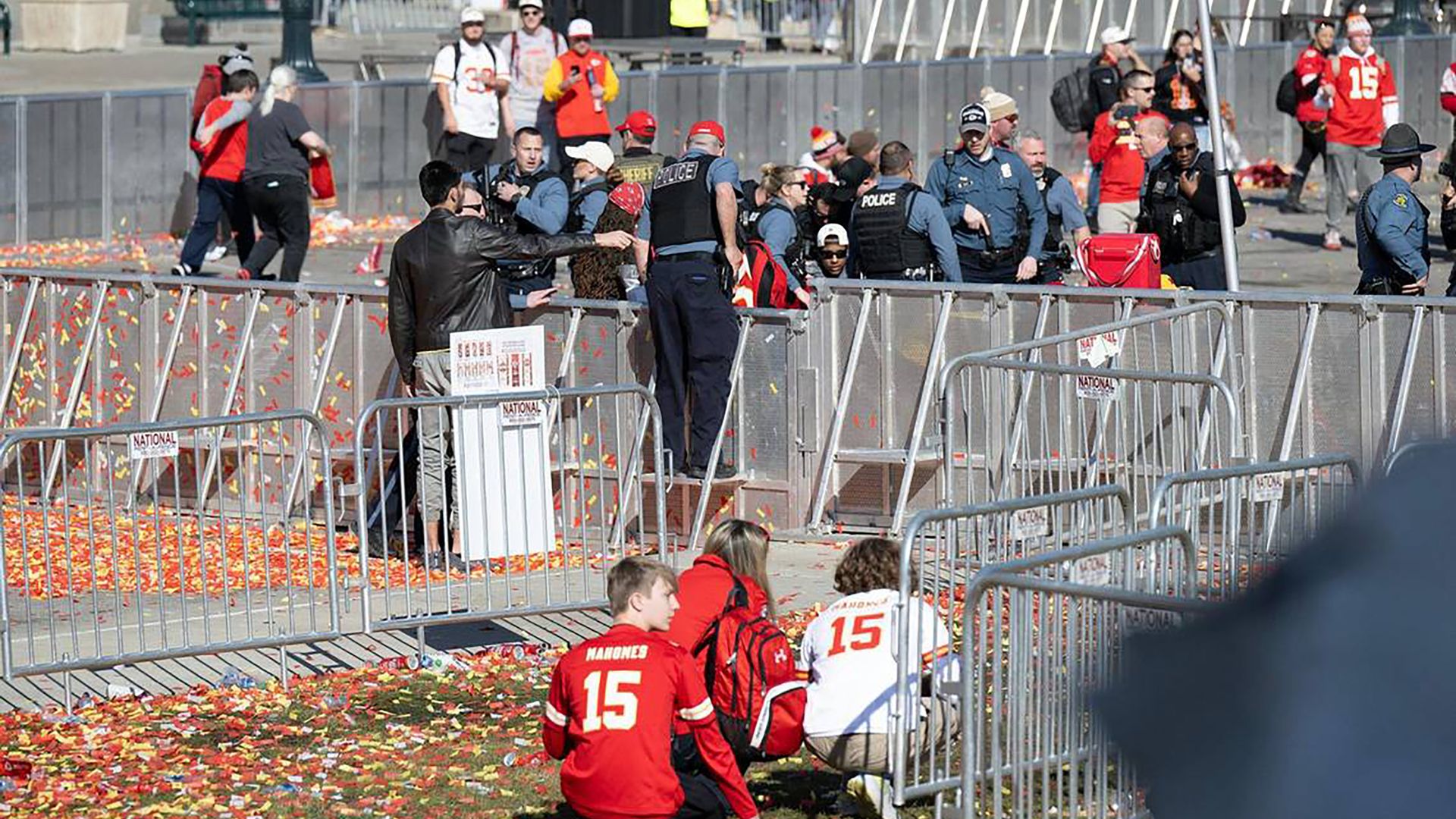 Multiple people in KC Chiefs apparel are seen among police officers outdoors.