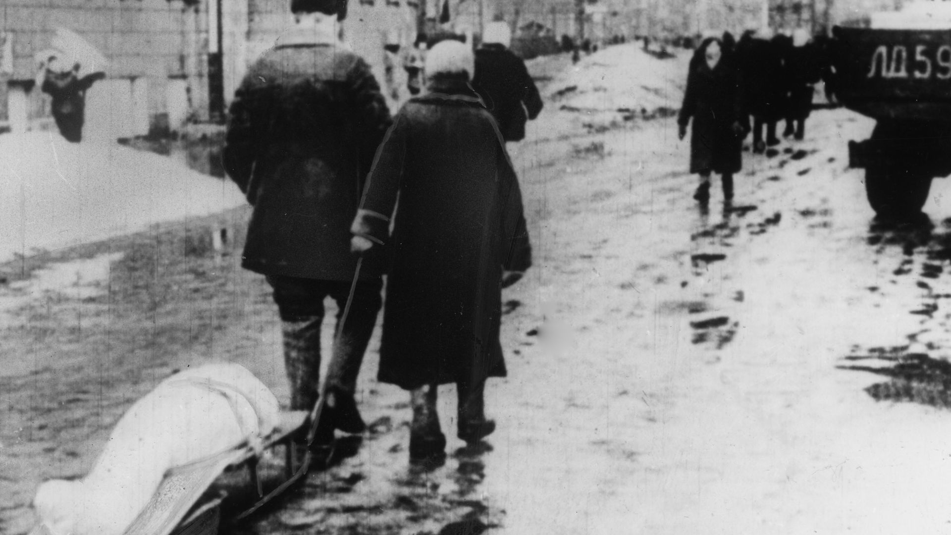 Black and white picture of two people carrying a corpse covered by w white sheet