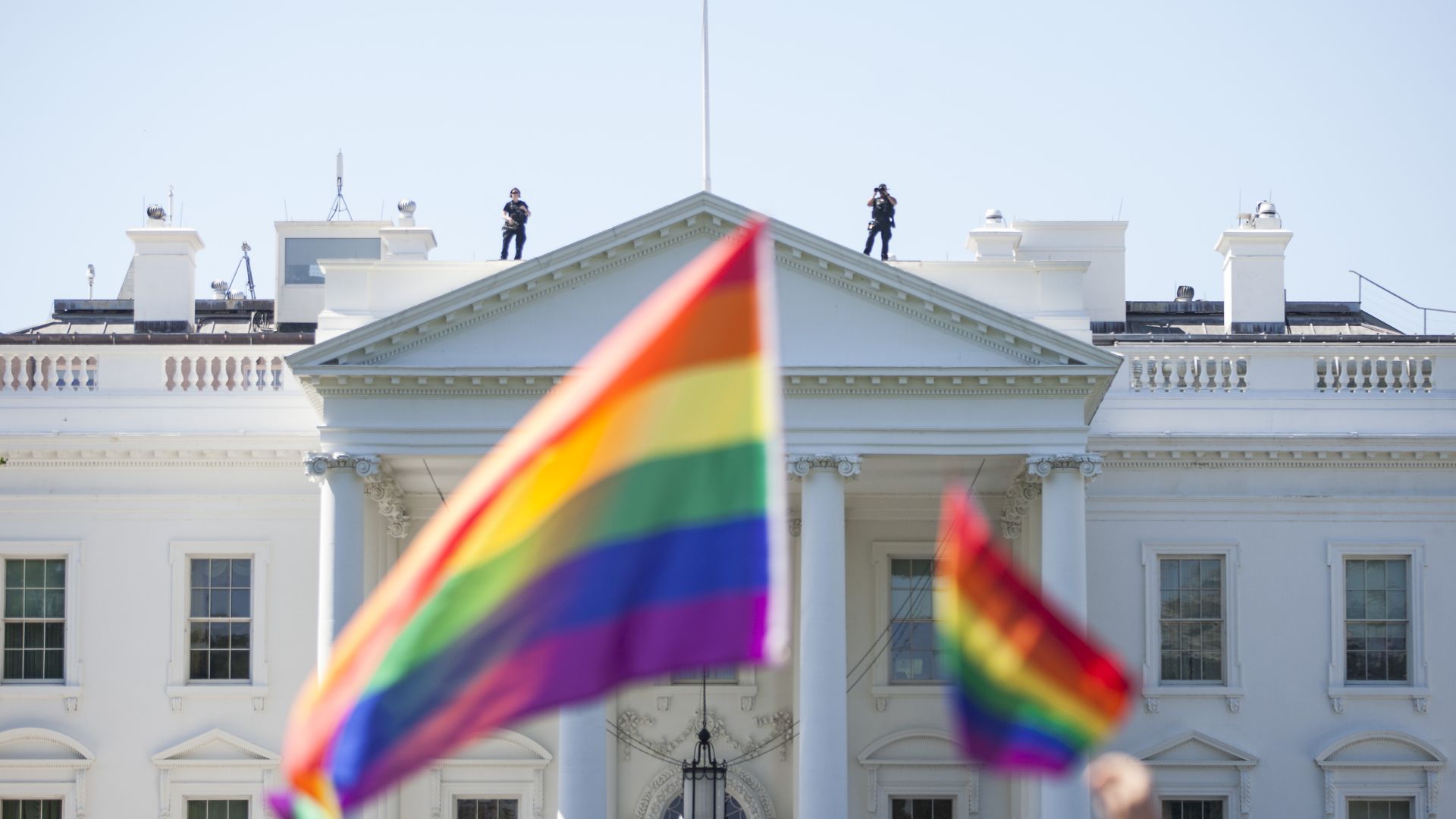 Rainbow flags in the foreground of a shot of the White House' south lawn
