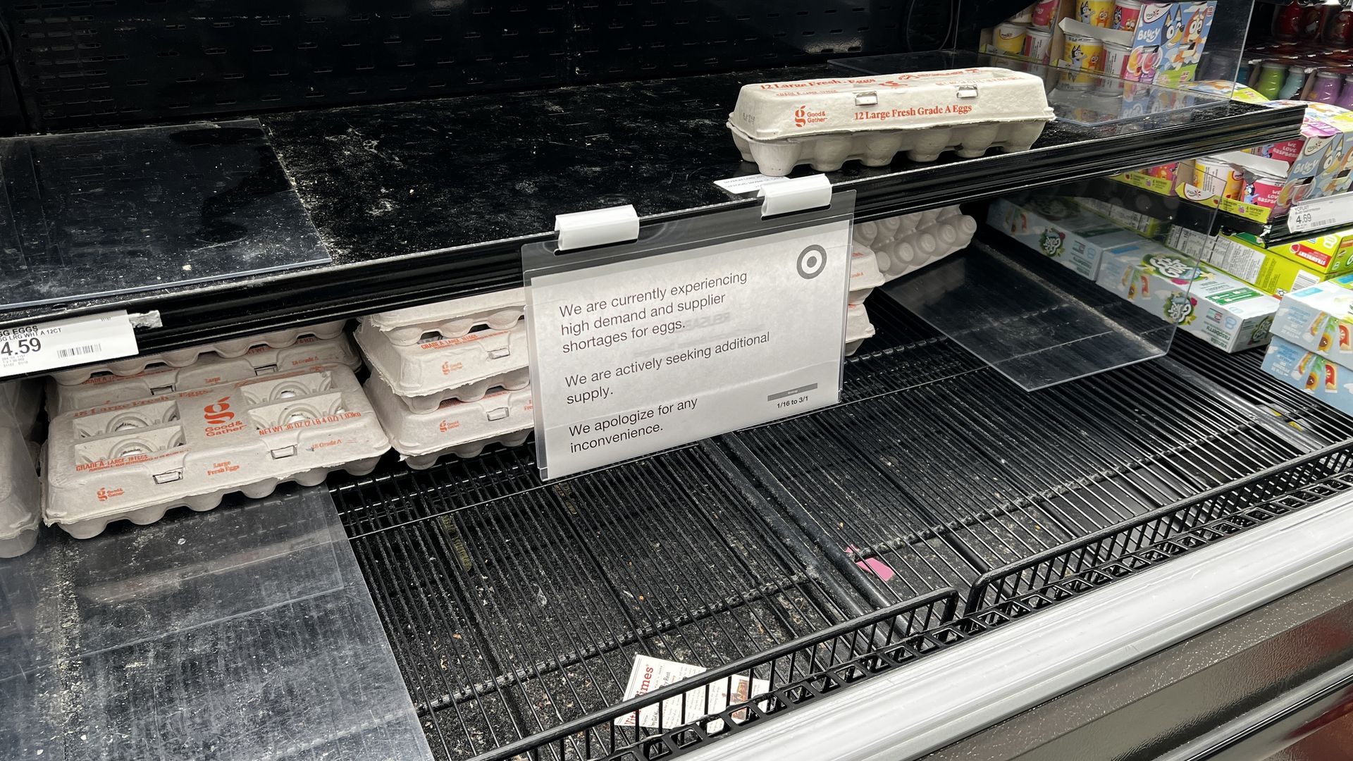 A sign at an egg station in target saying they are short in supply surrounded by a limited number of eggs.