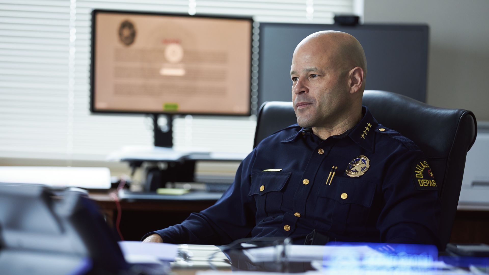 A man wearing a blue police uniform sits on a desk
