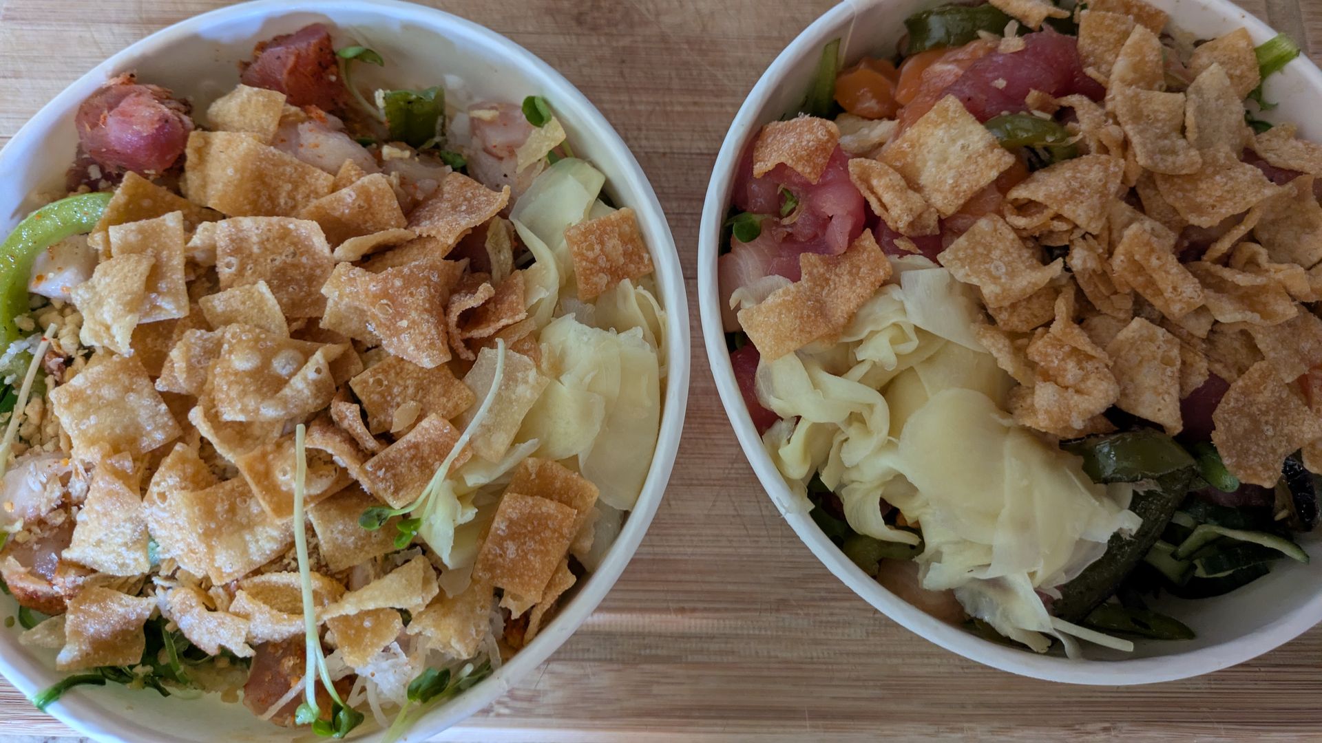 Two white bowls filled with taco salad on a wooden board: shredded lettuce and cabbage, diced meat, green peppers, and a generous topping of crispy tortilla chips.