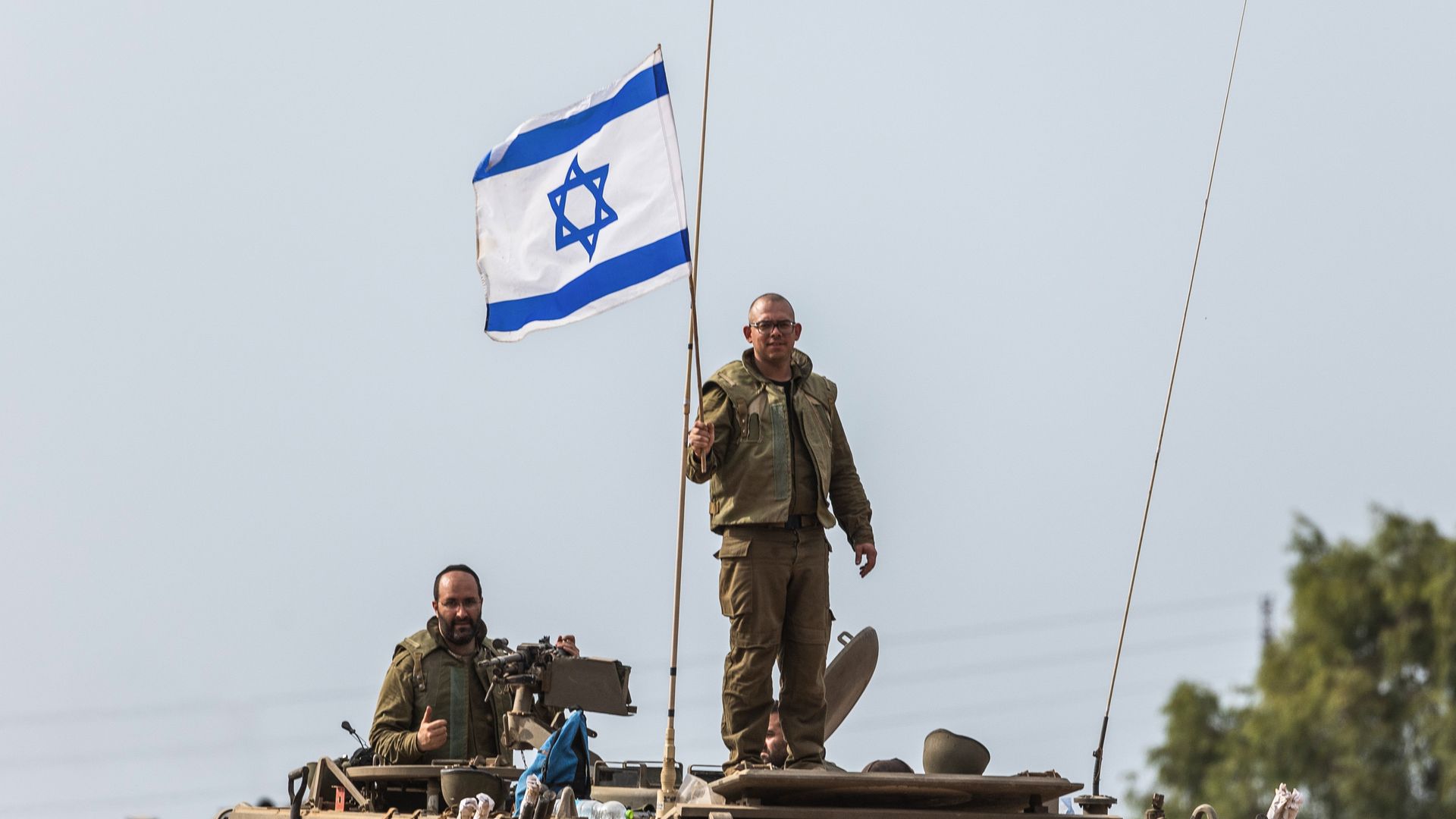 An Israeli military member stands above a tank holding up the Israeli flag as another sits nearby on the tank. Artillery forces are deployed near the Israel-Gaza border as fighting with Islamist Hamas militants continues.