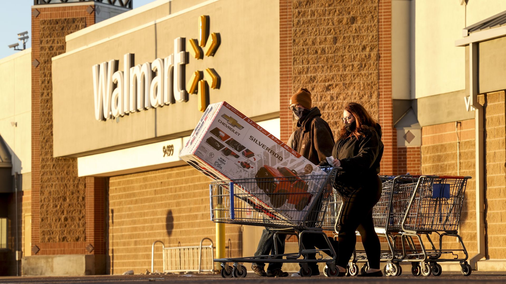 Shoppers pushing a cart with a toy ride-on car in front of a Walmart store