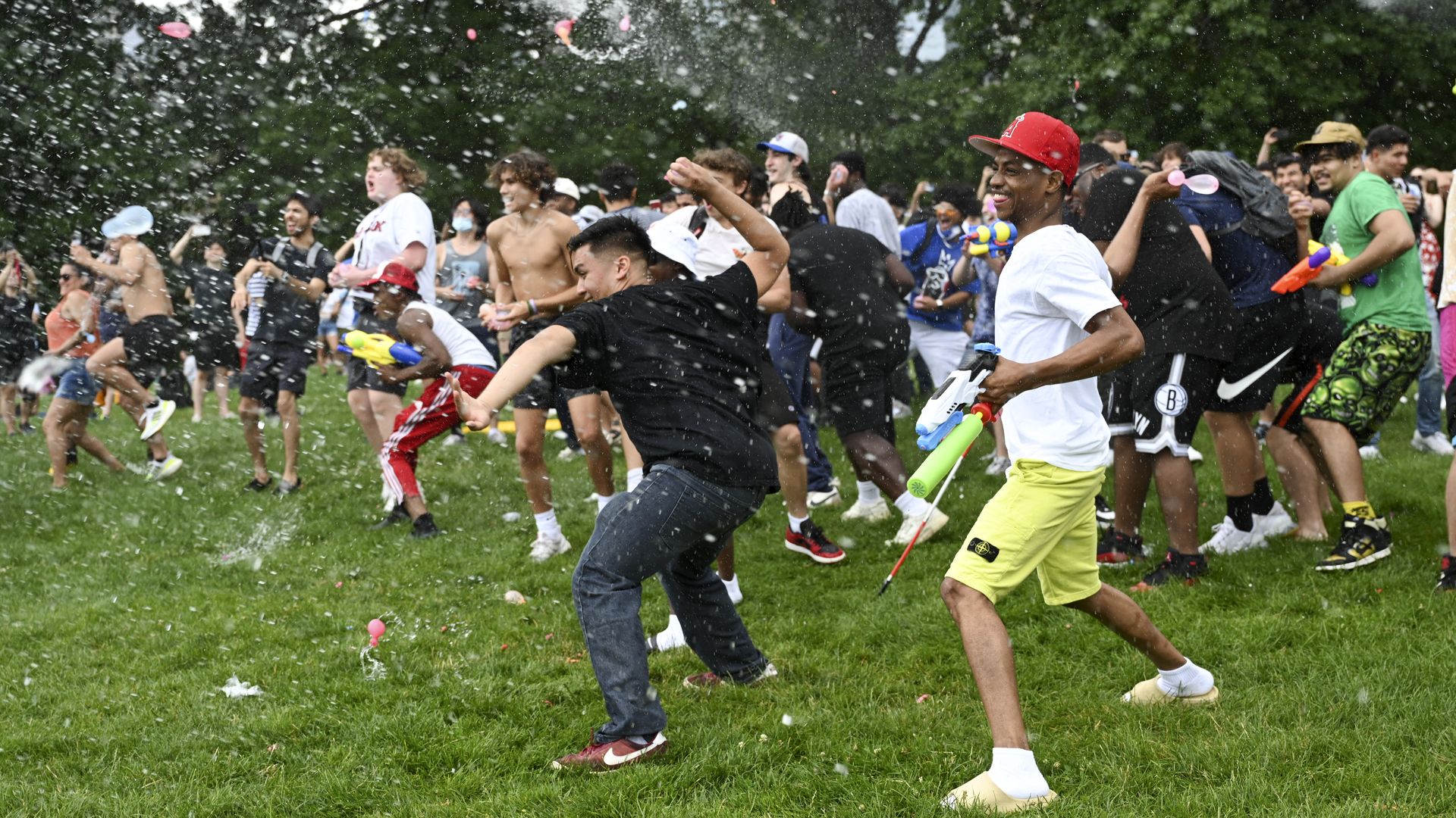 a group of people in a park throwing water balloons at each other.