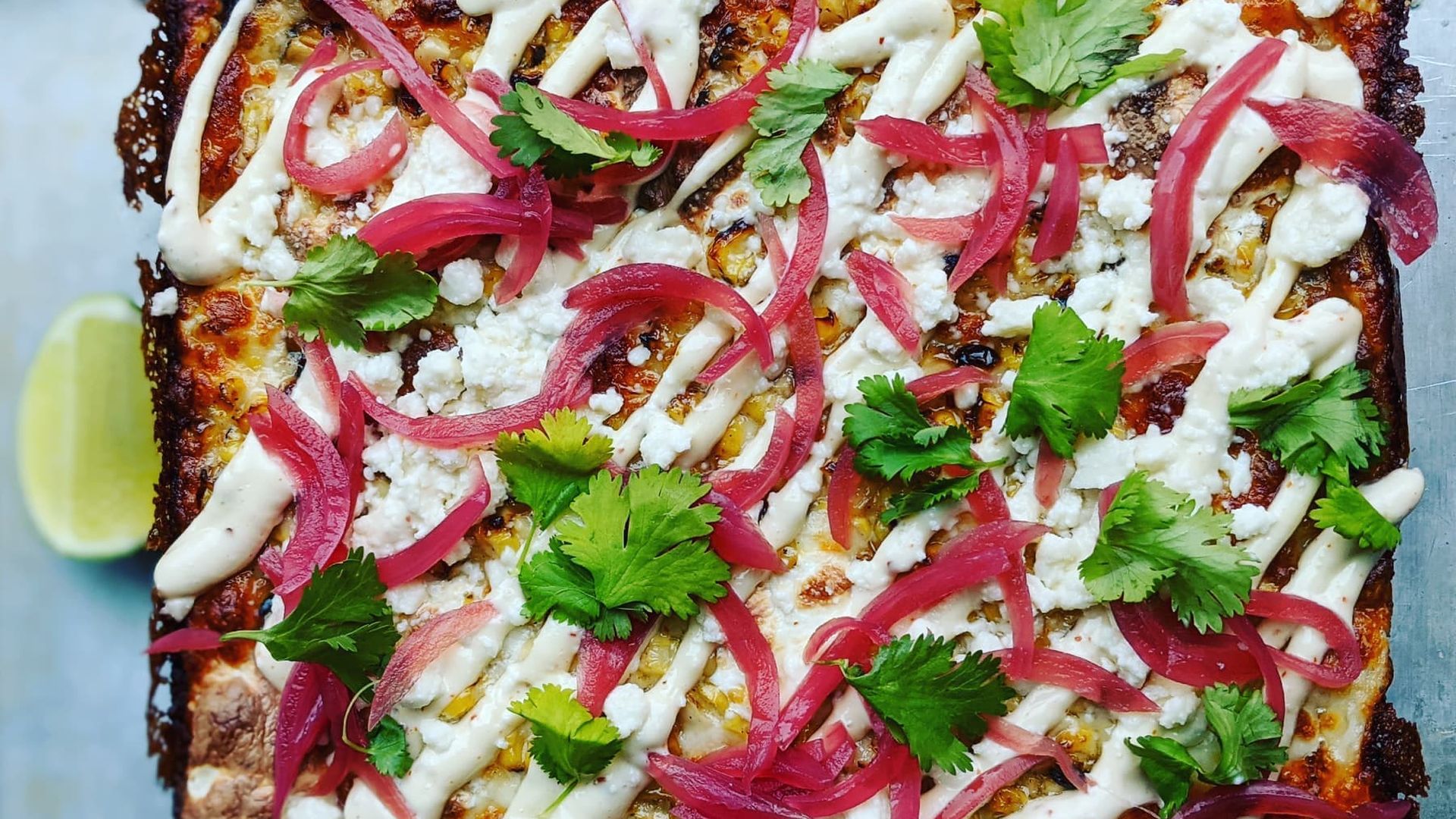 A rectangular pizza with pink and green toppings.