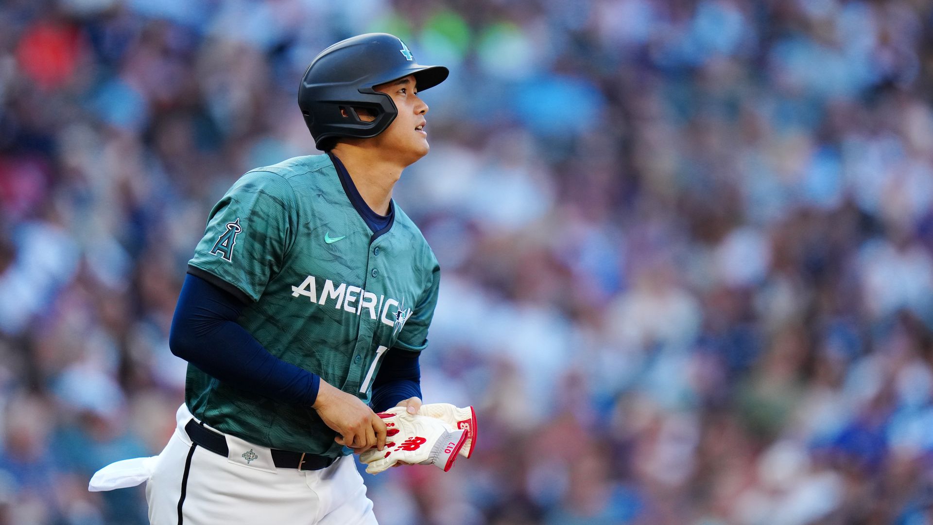 Shohei Otani in an American League All-Star Jersey and a helmet holds a glove, with a crowded stadium in the background.
