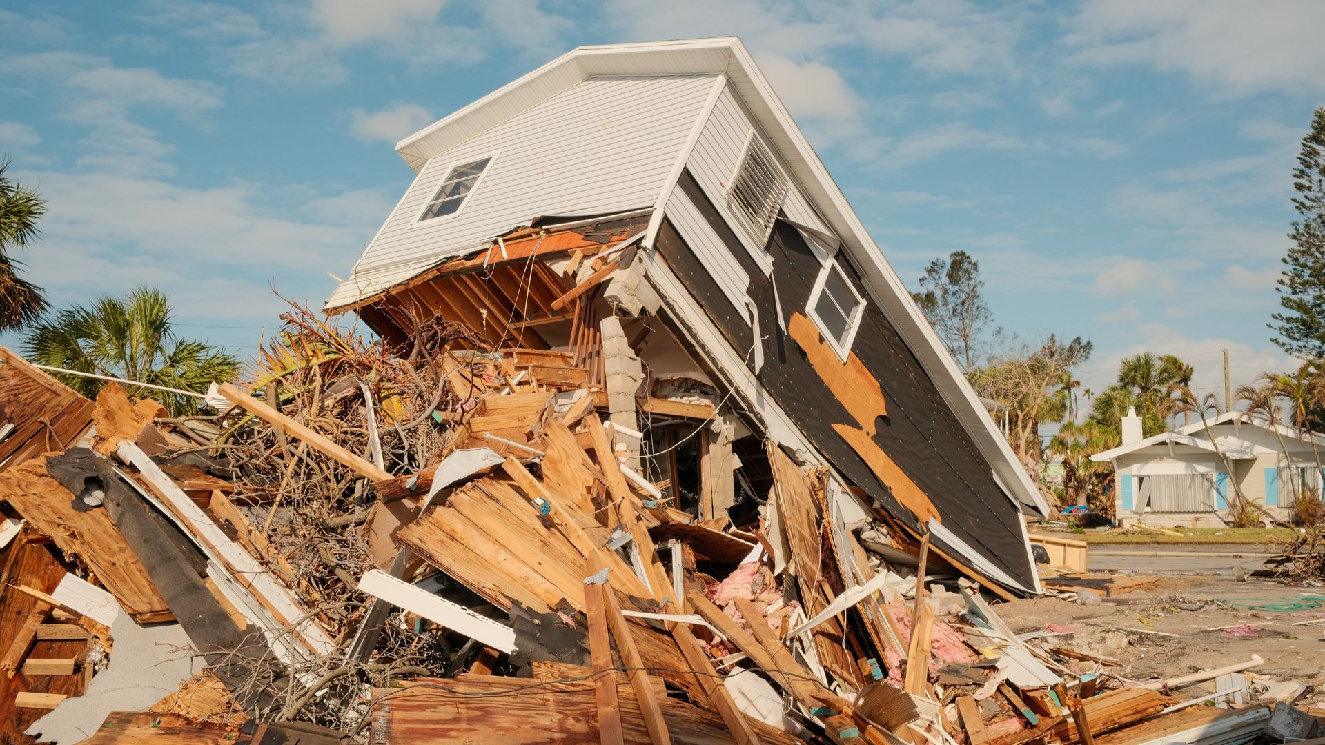 Photo of a house destroyed with several pieces of wood surrounding the broken frame