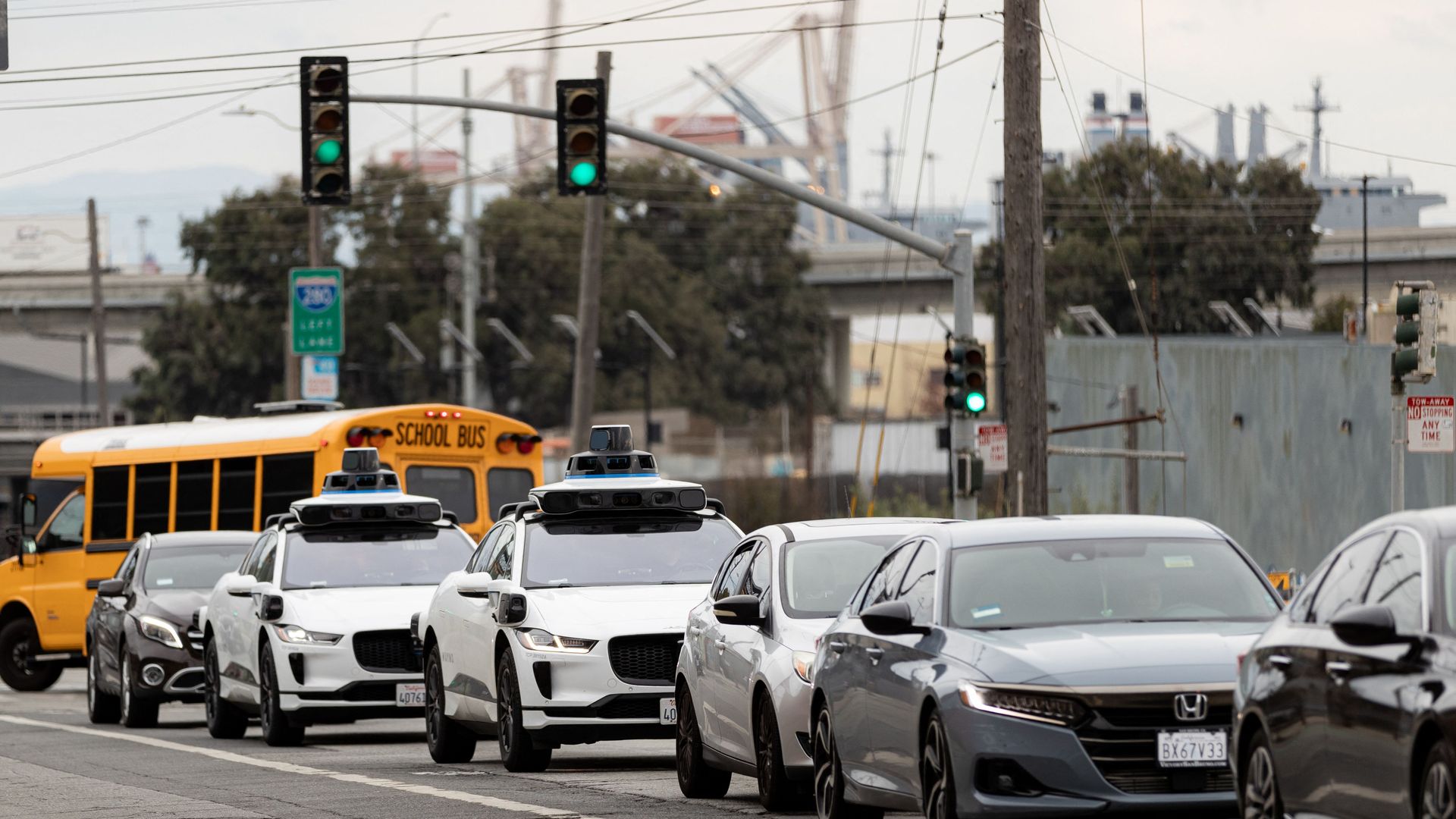 A line of traffic, including two Waymo robotaxis and a school bus