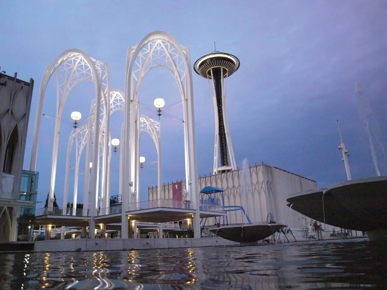The white arches of the Pacific Science Center above a pool of water with the Space Needle in background. 