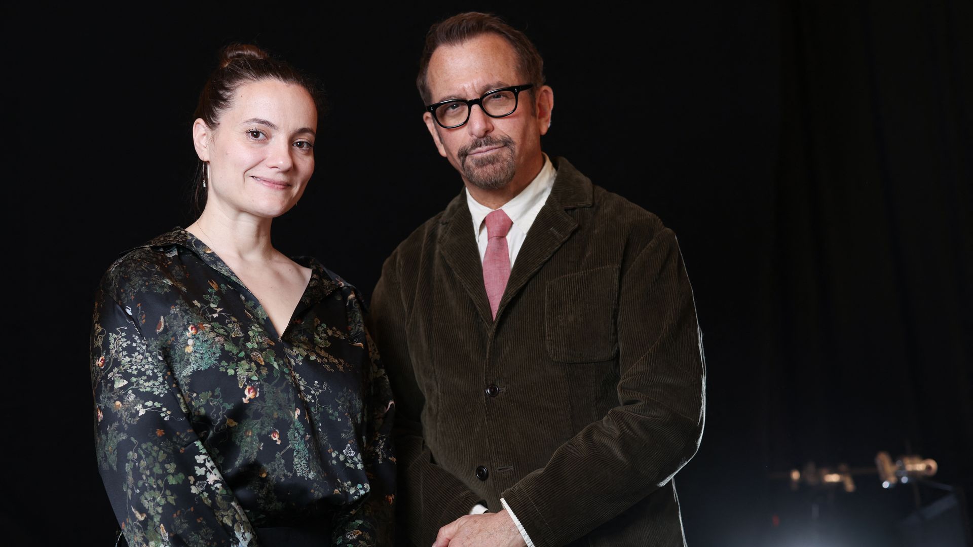 A man and woman stand facing the camera against a nighttime backdrop.