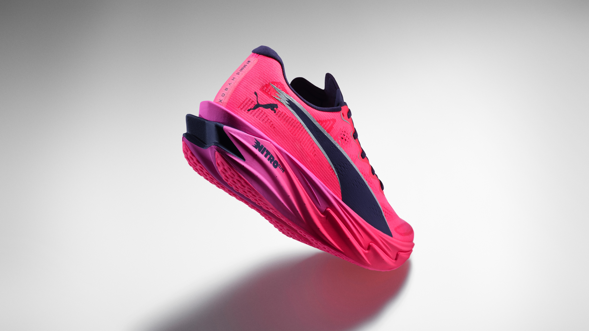 Bright pink Puma Nitro Elite running shoe with dark navy accents, floating against a neutral gray background casting a soft shadow below.