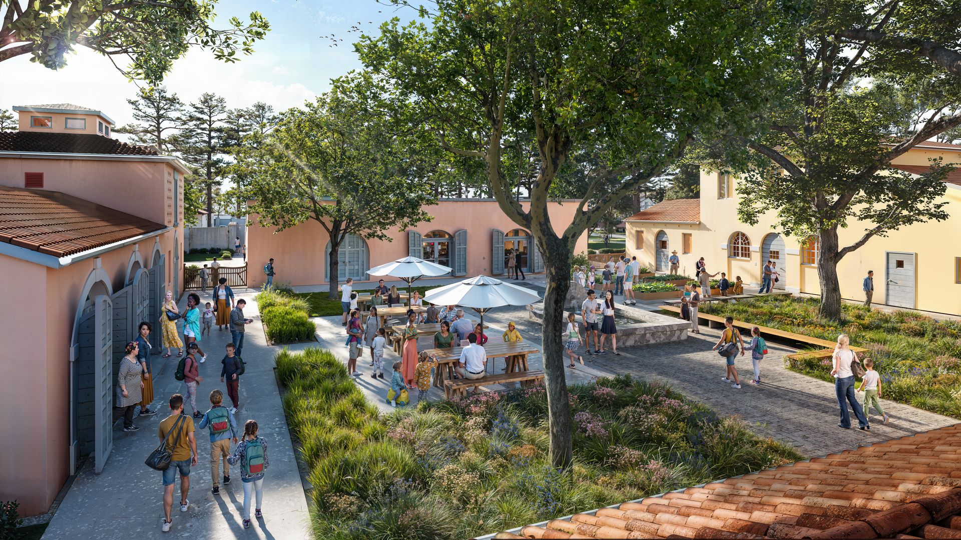 Sunlit courtyard framed by pastel houses and tall leafy trees, with outdoor tables and umbrellas. People stroll, chat, and children play along a brick-paved path.