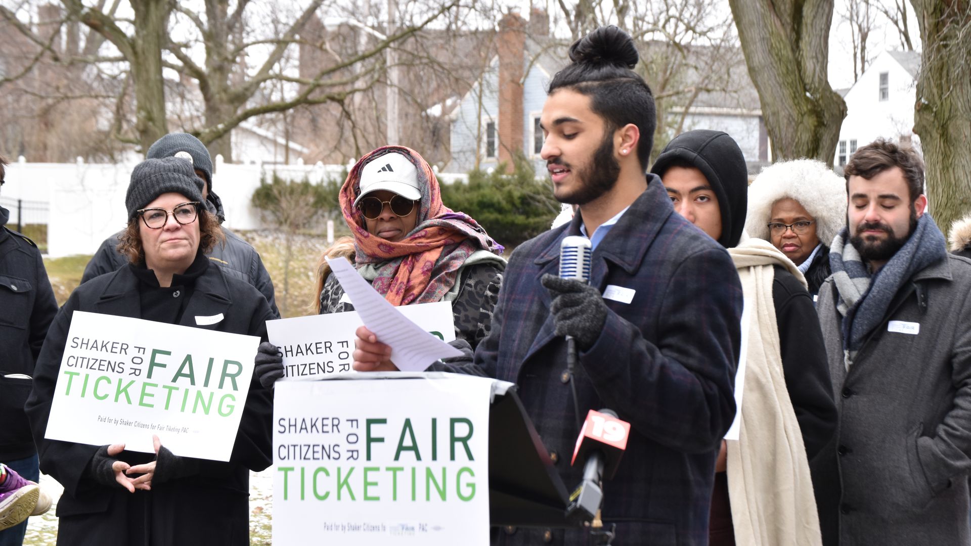 17-year-old Ethan Khorana reads from a paper at outdoor event launching Shaker Citizens for Fair Ticketing event. People in jackets stands behind.