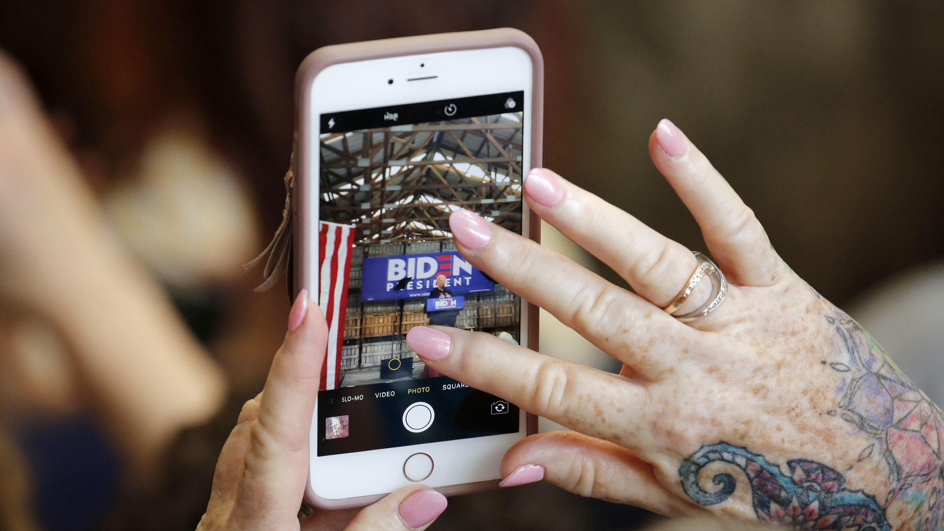 A photo of a woman's hands holding a smartphone, which displays Joe Biden giving a campaign speech.