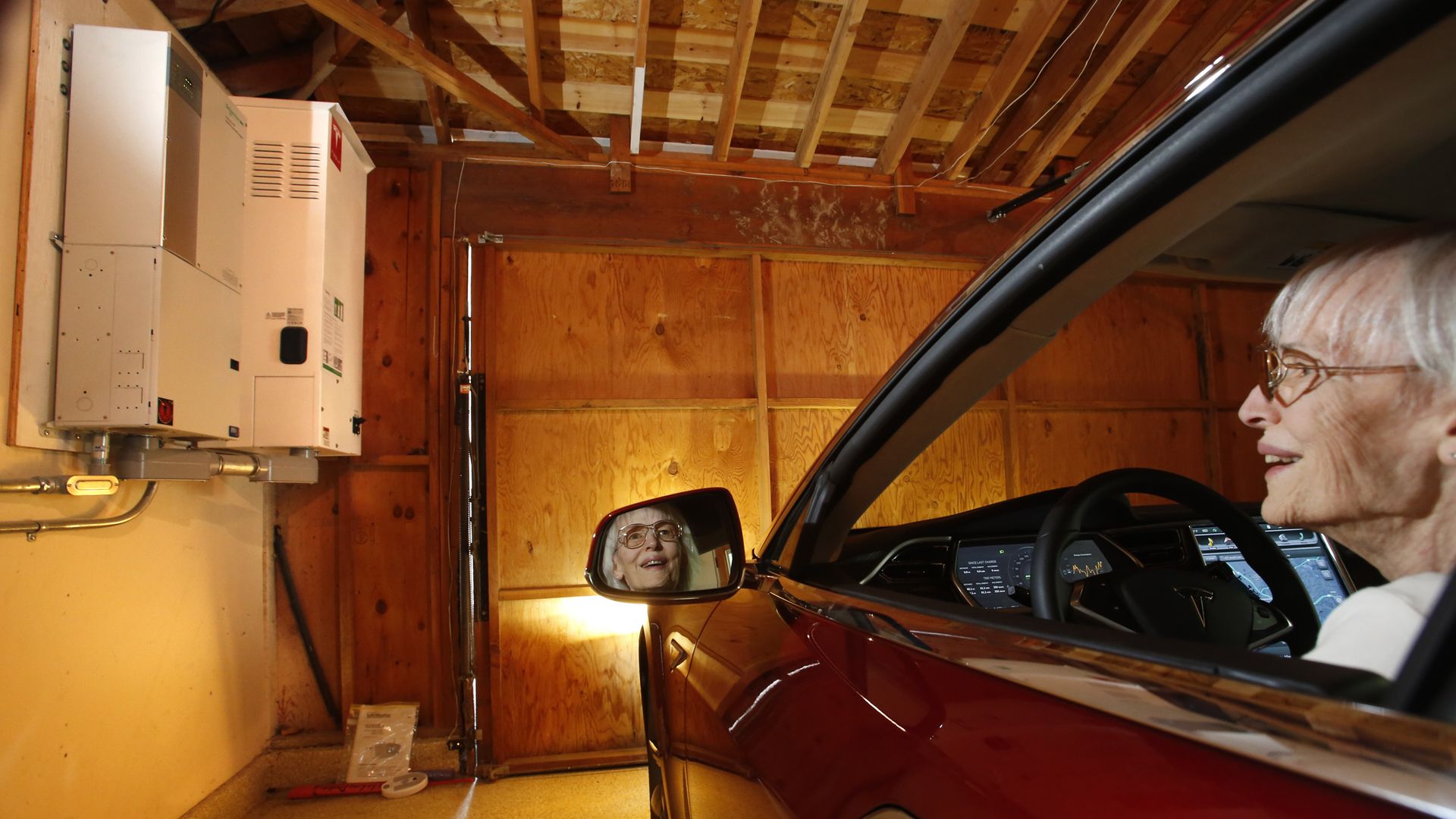 In the garage of her solar powered home, Cassina Tarsia looks at the large battery on the wall that stores electricity charge her Tesla all-electric car.