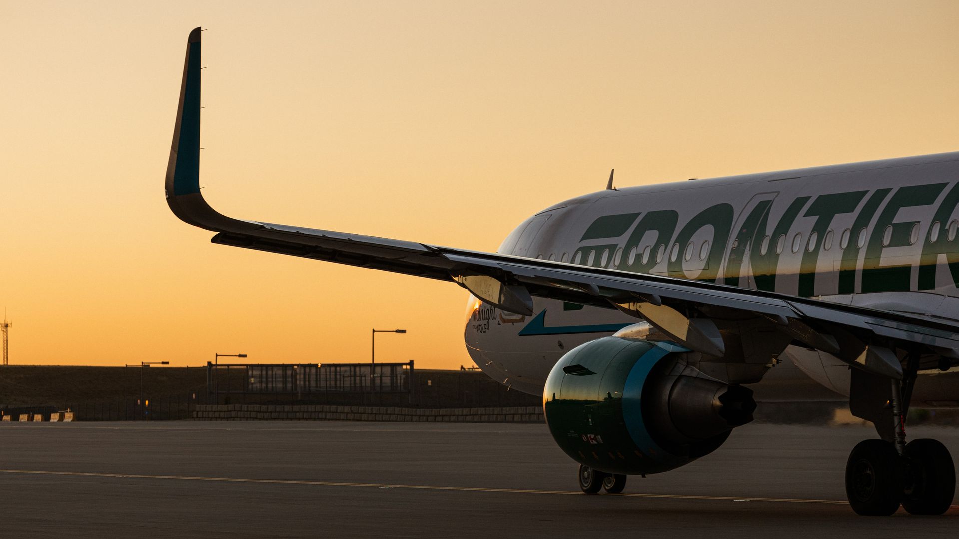 Close-up of Frontier Airlines airplane wing and engine on runway during a golden sunset with orange sky in the background.
