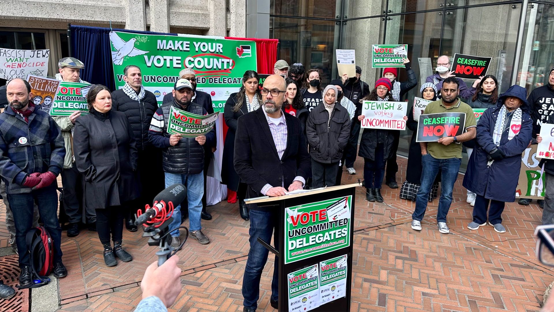 People, some with political signs, standing in front of a building. 