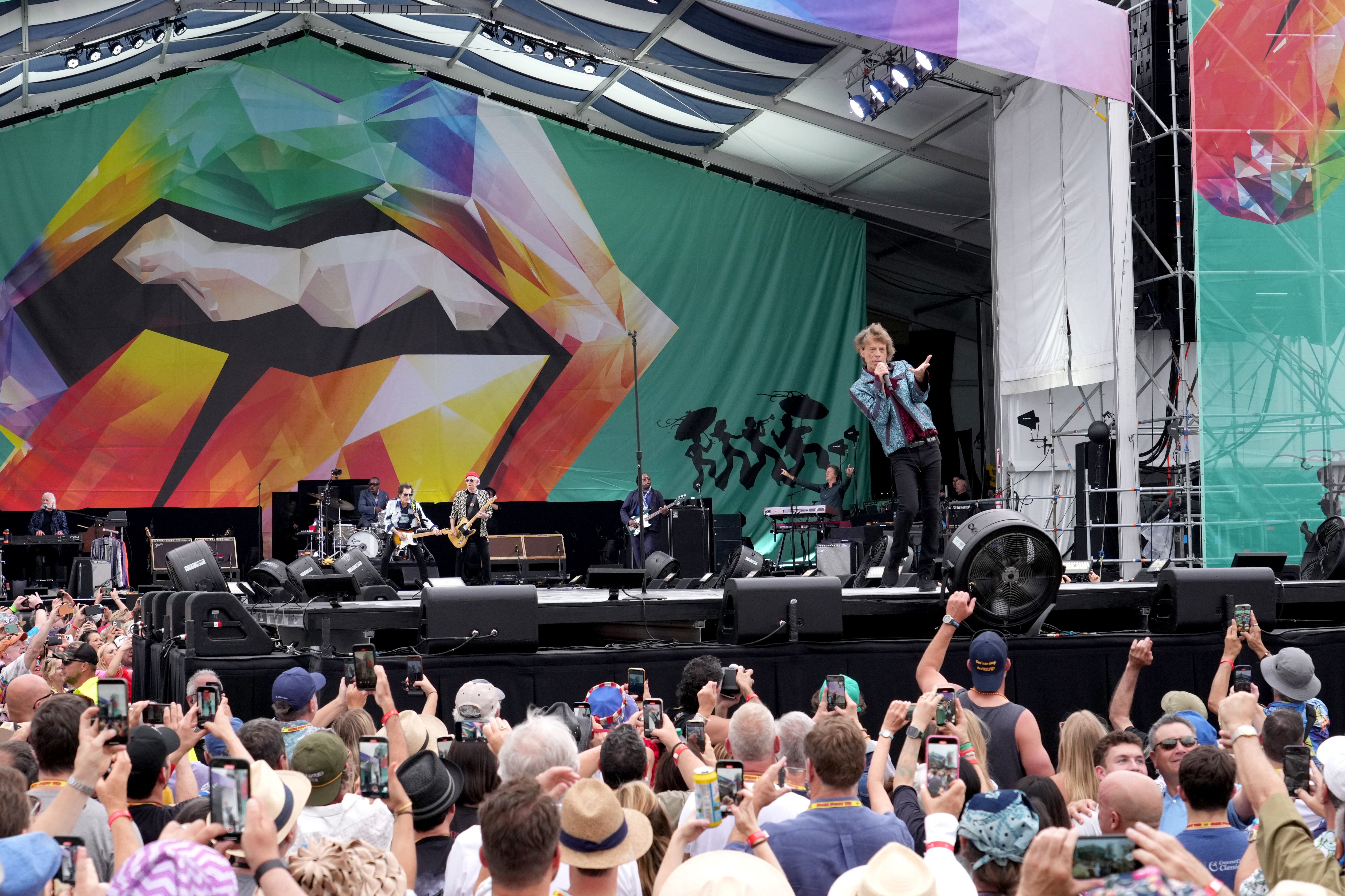 Mick Jagger performs on a Jazz Fest stage as a crowd looks on. The Stones' logo is on the stage backdrop  behind him.