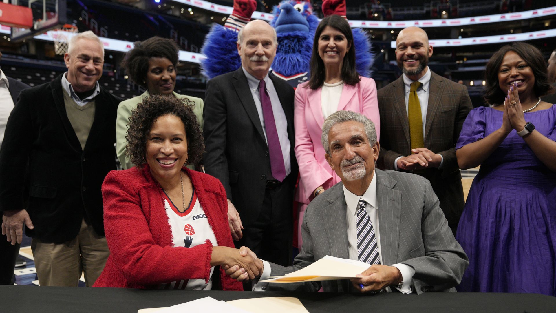 Muriel Bowser and Ted Leonsis shake hands smiling after signing a deal 