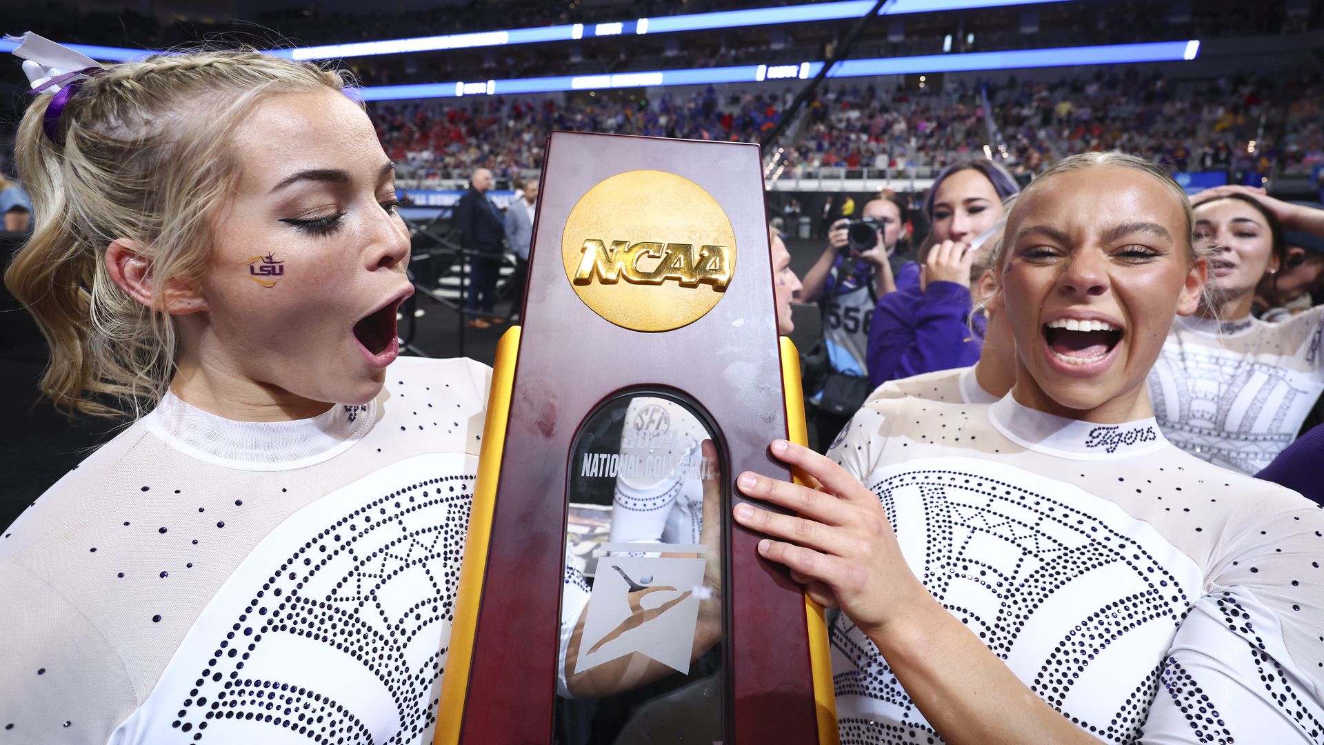 Olivia Dunne and Chase Brock hold up the NCAA Gymnastics Championship trophy while celebrating their team's win.