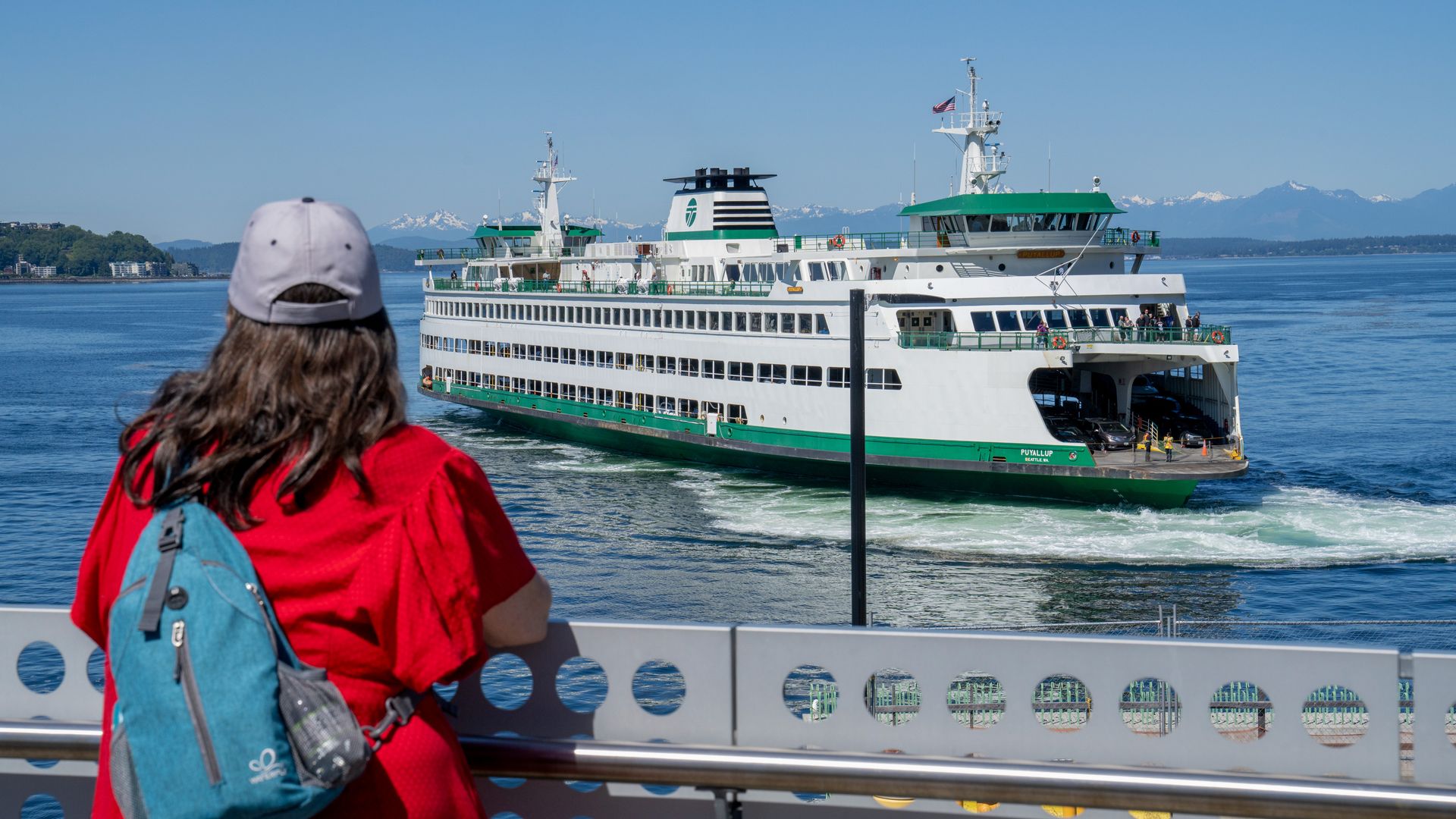 A ferry is shown in the water while a passenger looks on from the dock.